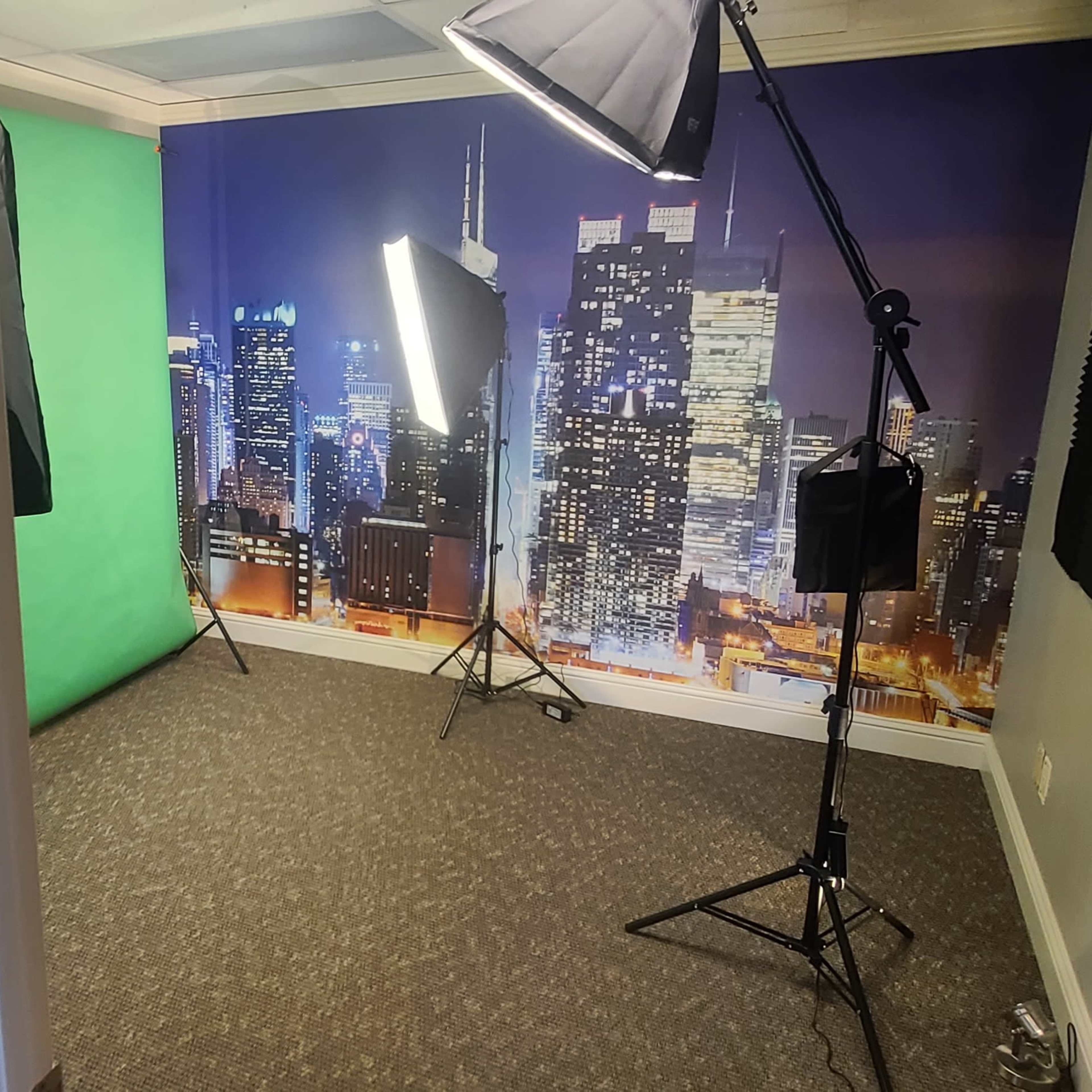 A studio setup featuring a green screen, softbox lights, and a city skyline backdrop.