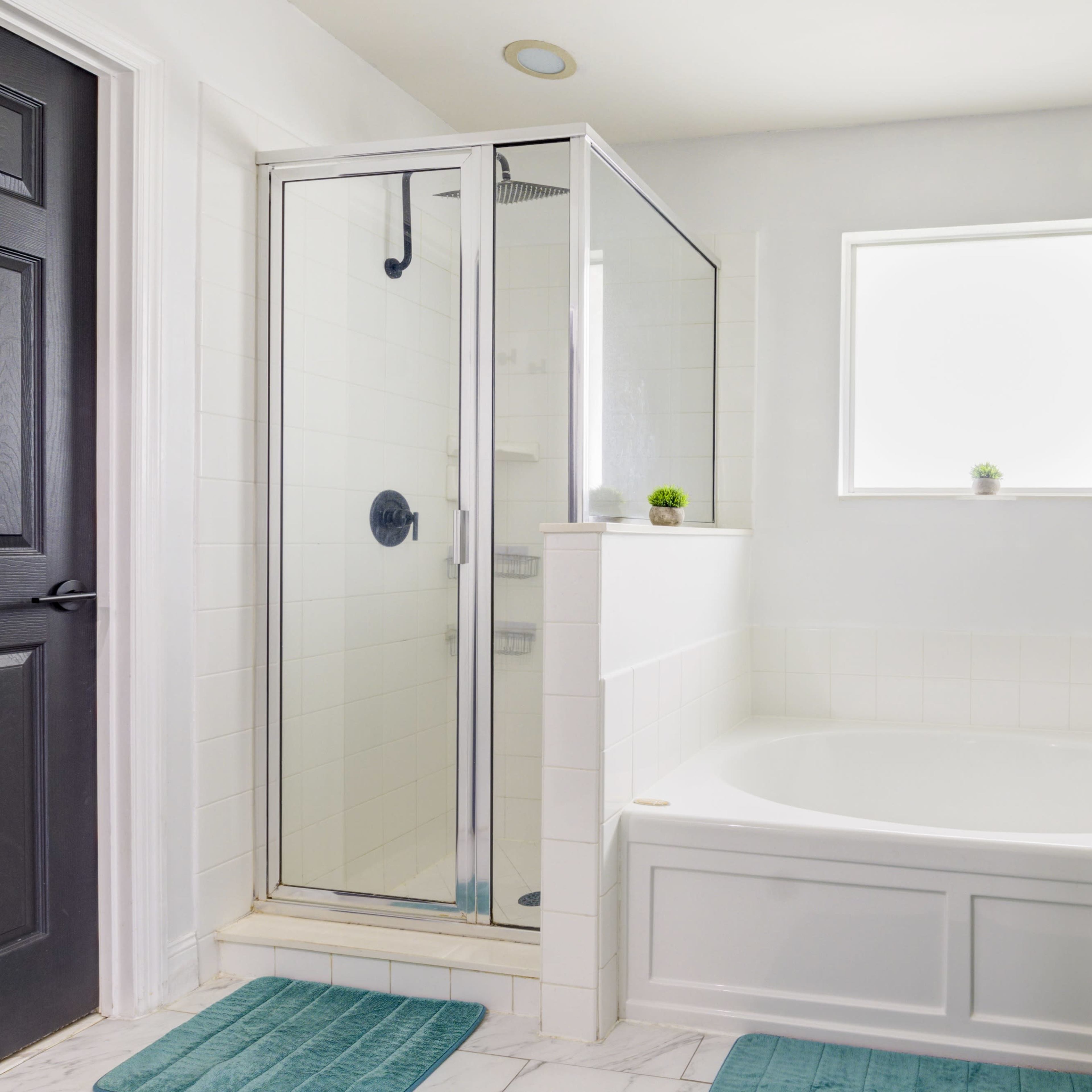 A modern bathroom featuring a glass-enclosed shower, a large bathtub, and a window above the tub.