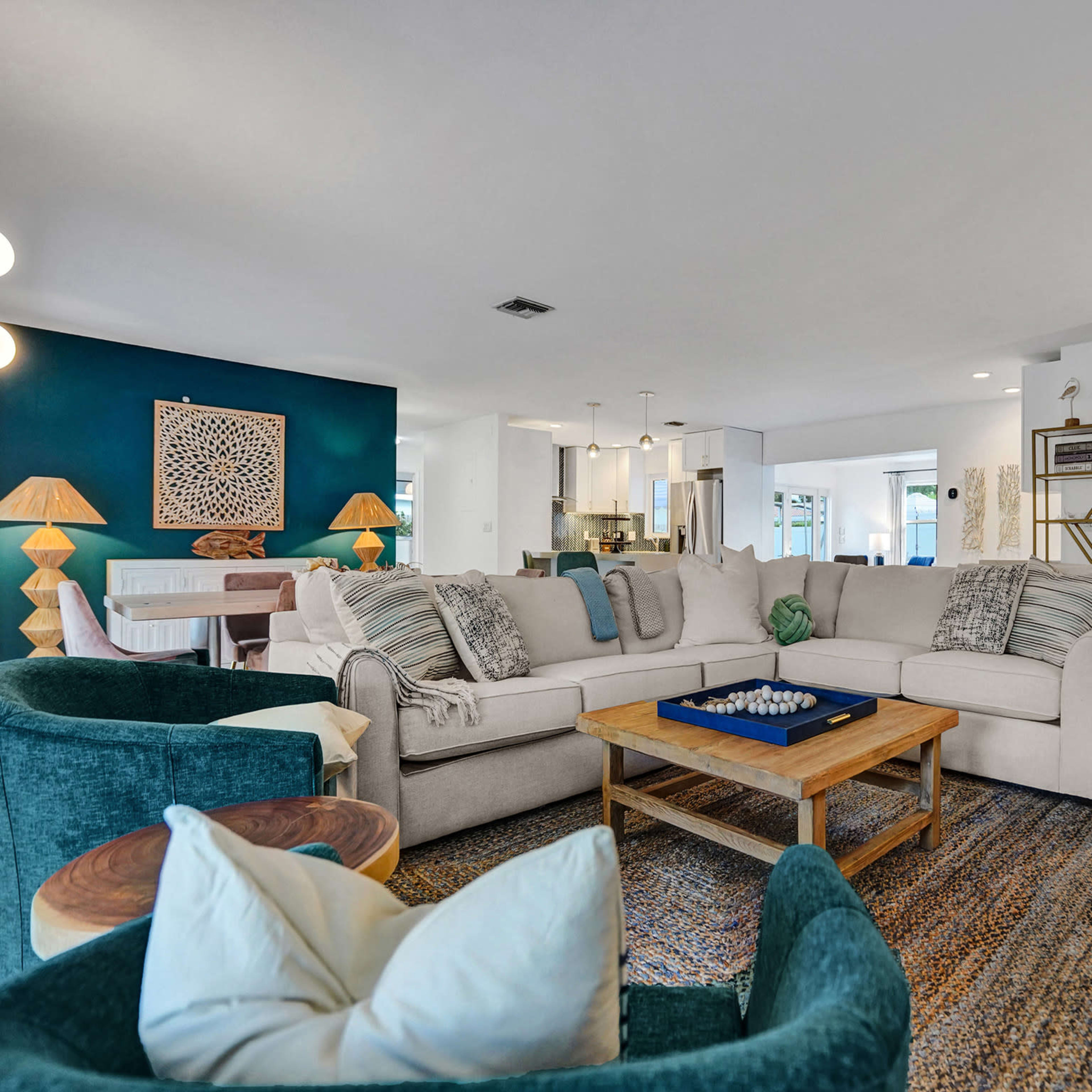 The spacious living room features a large sectional sofa, a wooden coffee table, and a mix of green chairs, with a dark accent wall and an open layout toward the kitchen.