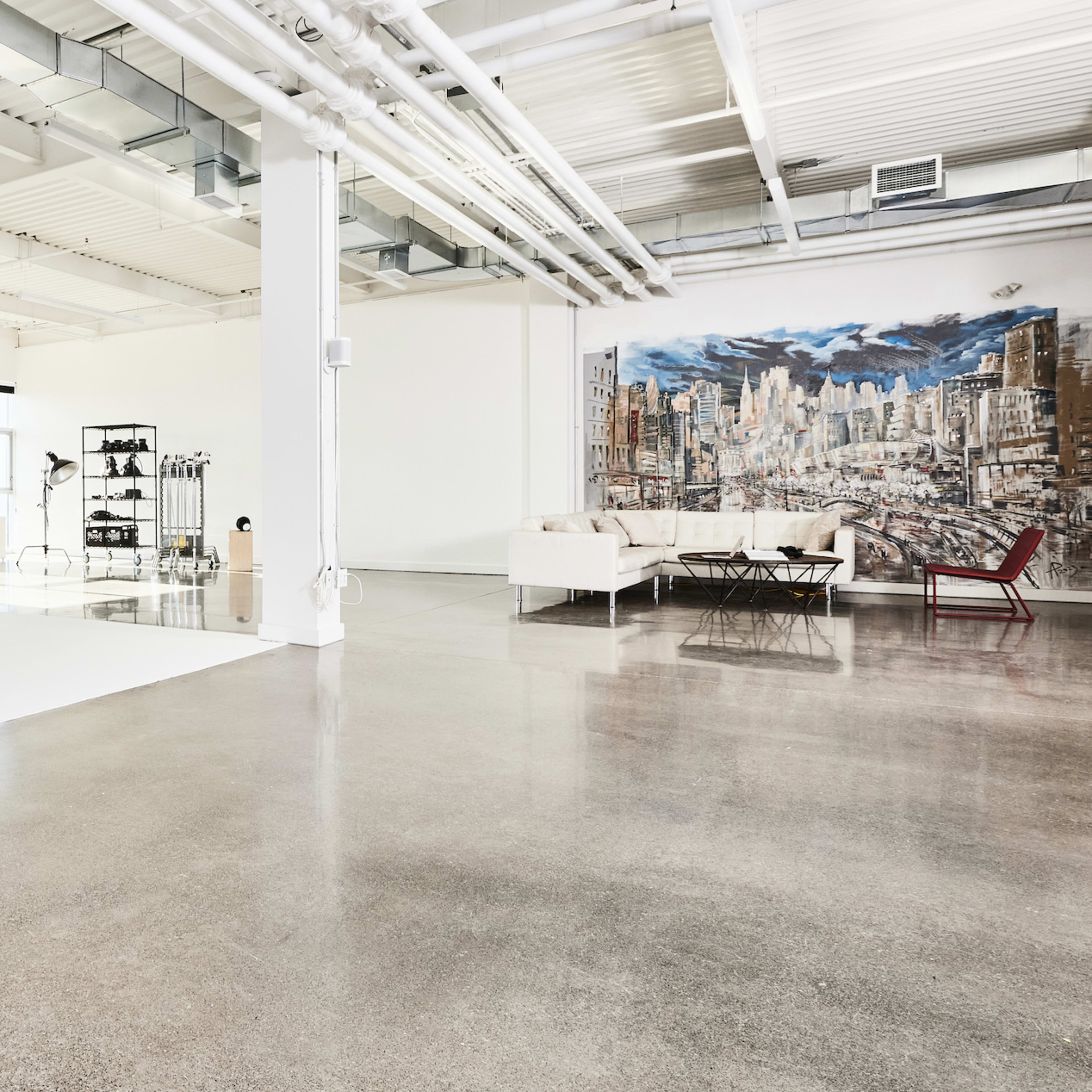 A spacious photography studio with various equipment, including softboxes and a backdrop, alongside modern furniture.