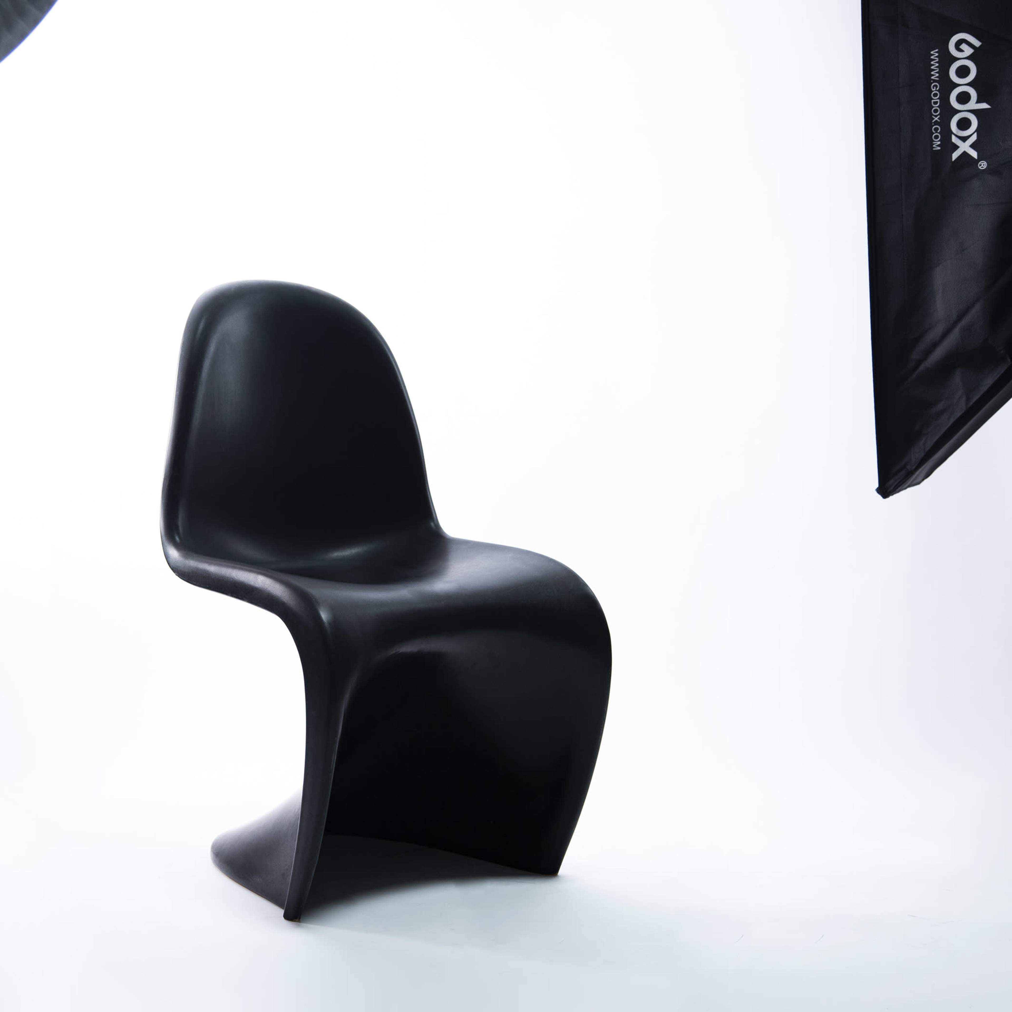 A black, modern chair placed on a light backdrop, accompanied by studio lighting equipment.