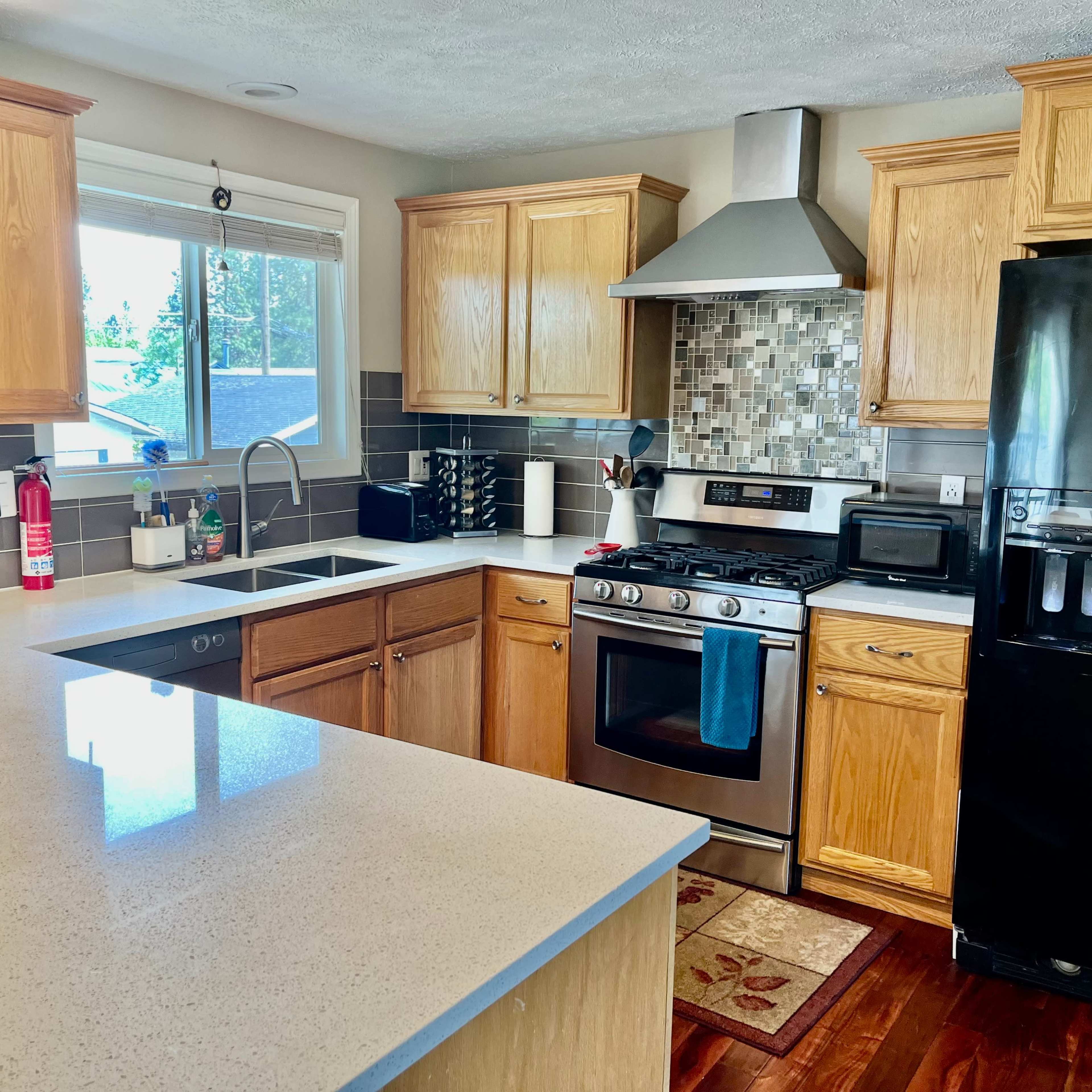 A modern kitchen features wooden cabinets, a stainless steel stove, a black refrigerator, and a countertop with a sink under a window.
