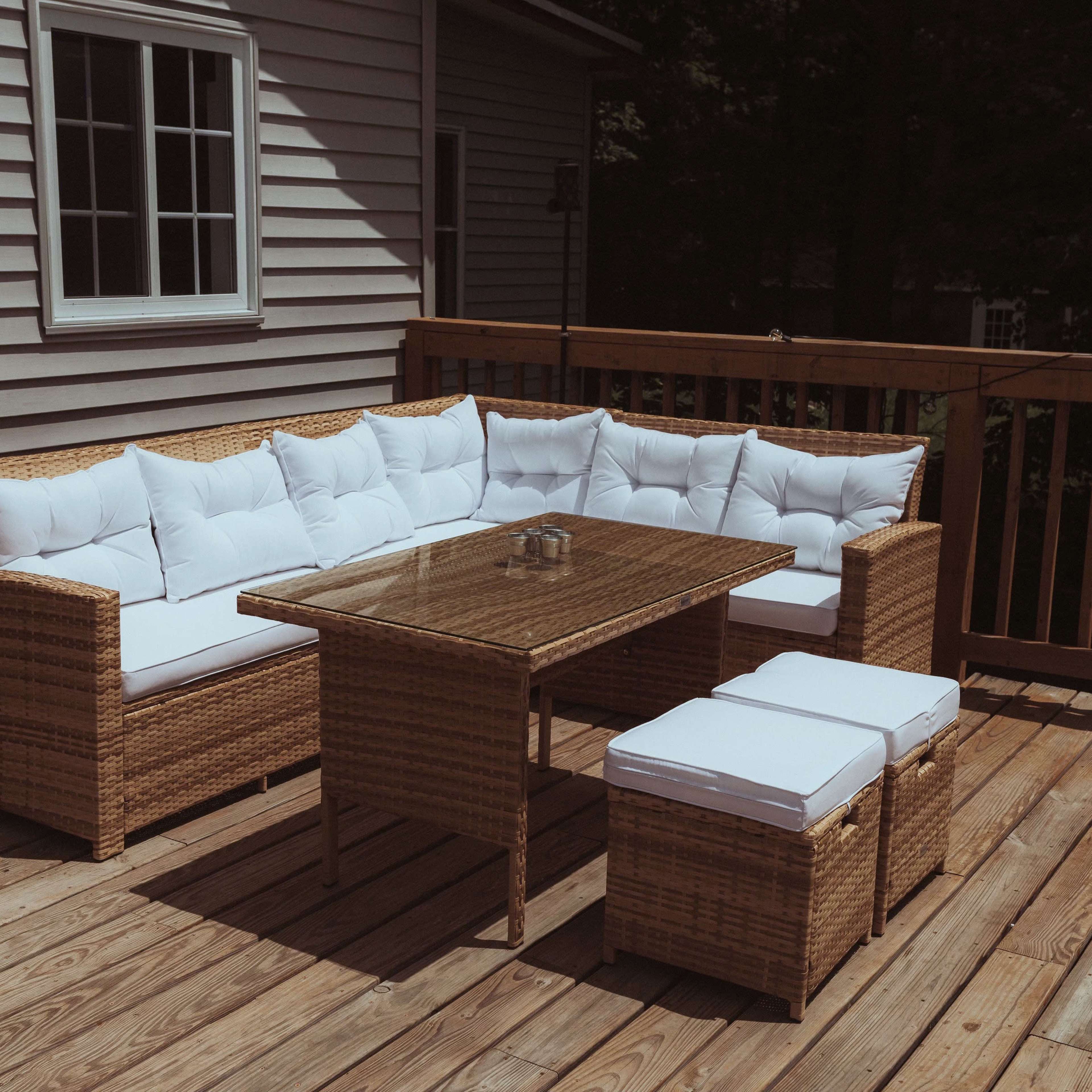 A wicker outdoor seating arrangement with white cushions and a glass-top table is positioned on a wooden deck.