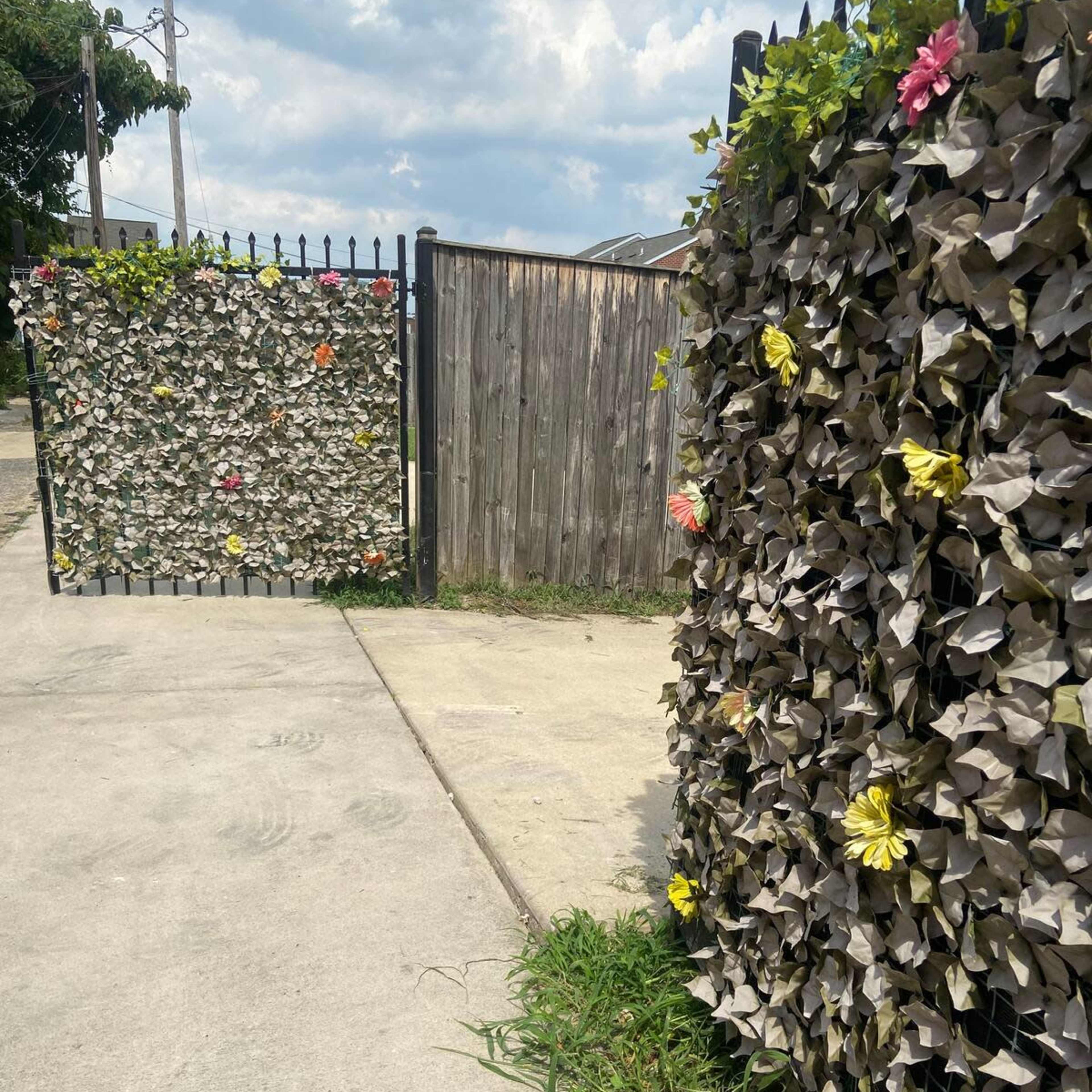 A pathway leads to a gated entrance adorned with colorful flowers and a textured metal wall.