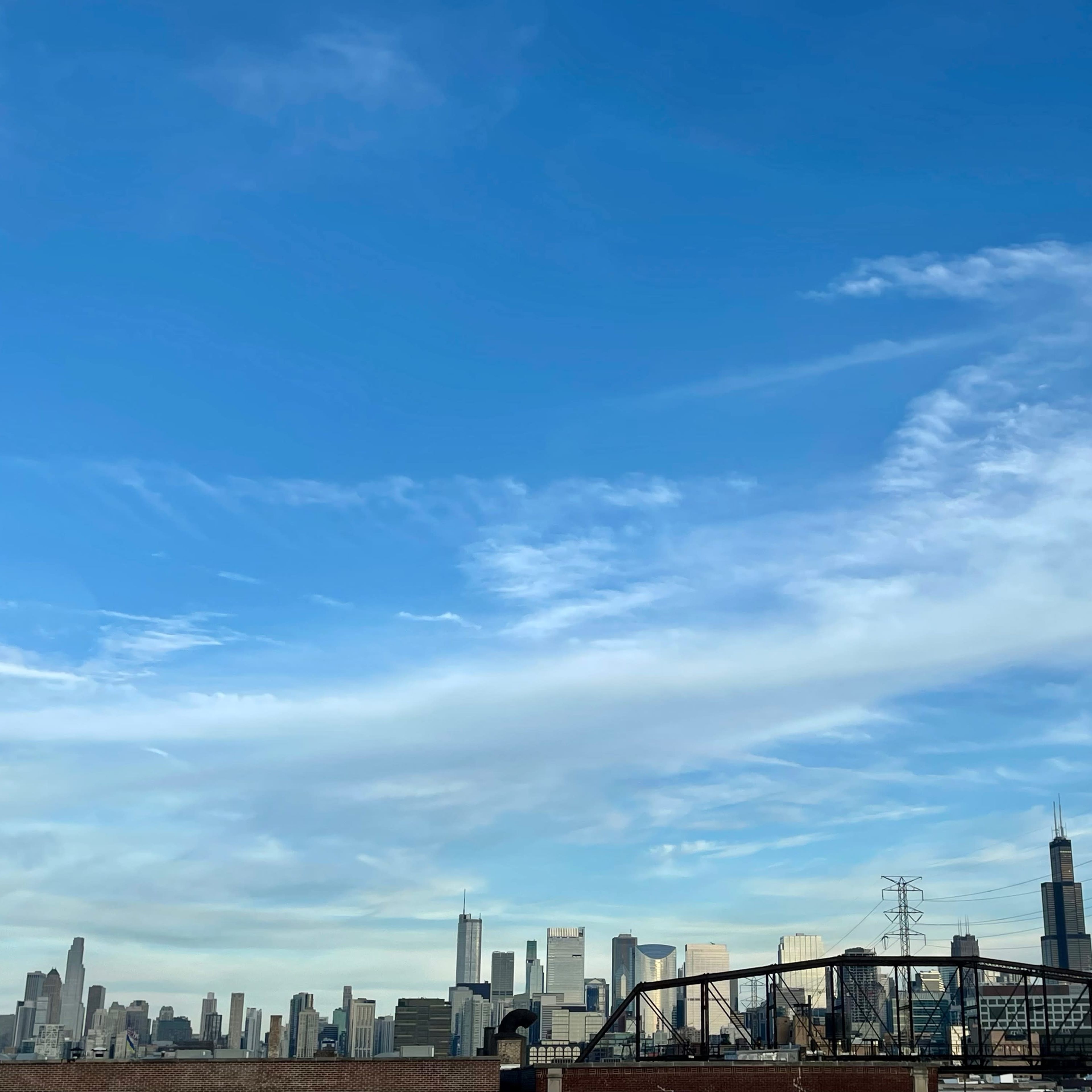 A skyline of a city with tall buildings under a bright blue sky and wispy clouds.