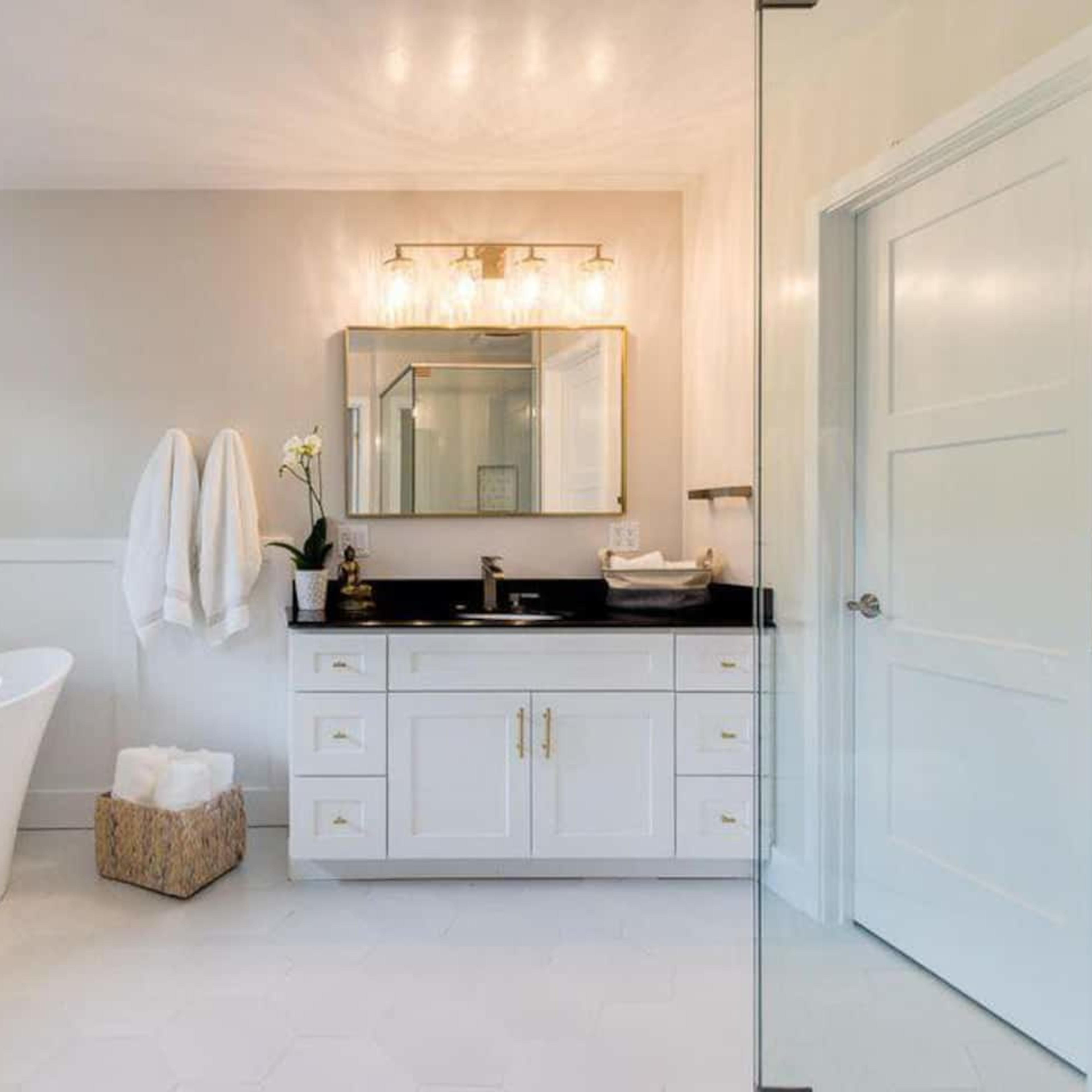 A clean, modern bathroom features a freestanding bathtub, a double-sink vanity with a black countertop, and white cabinetry against light-colored walls.