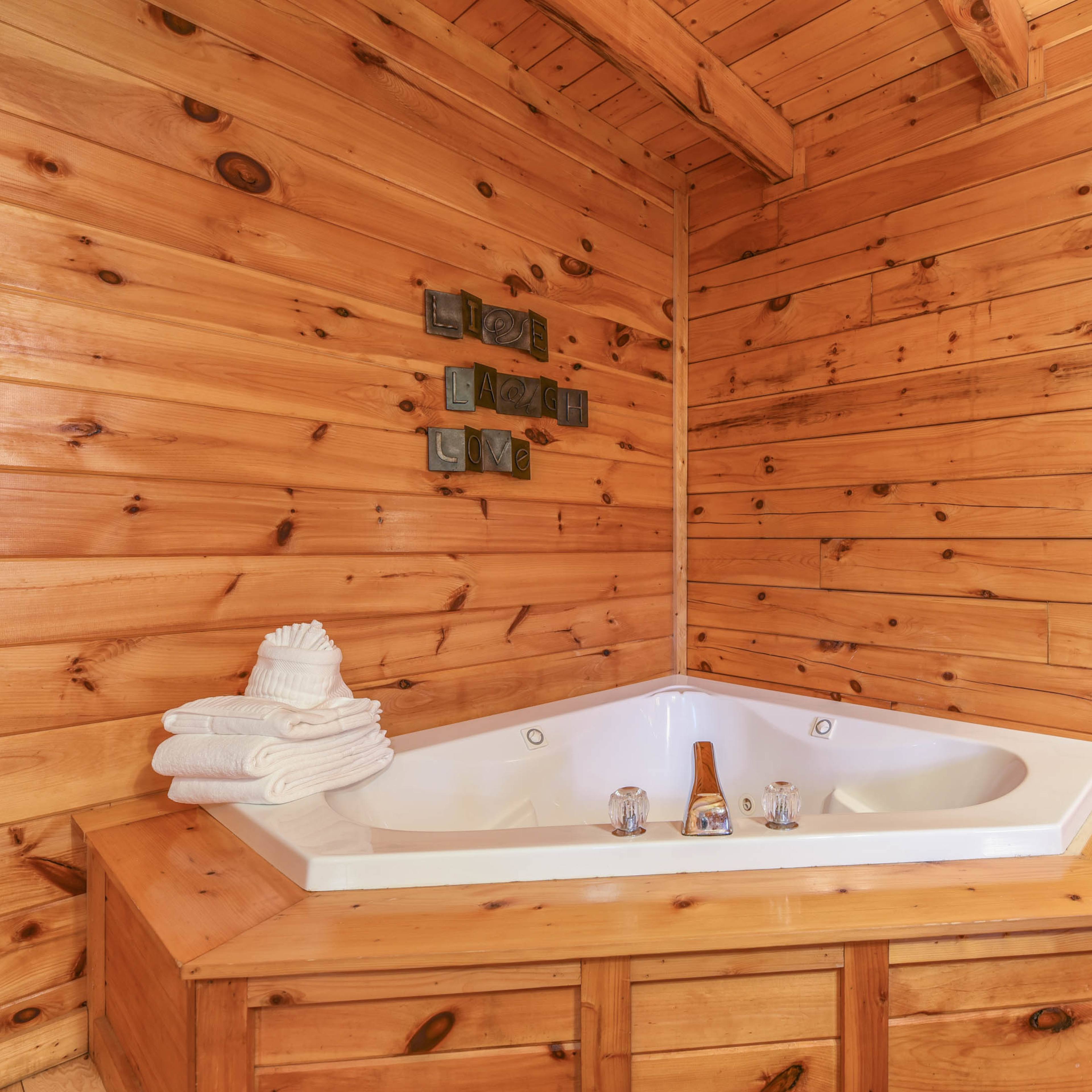 A corner hot tub surrounded by wooden walls and a shelf with neatly stacked towels.