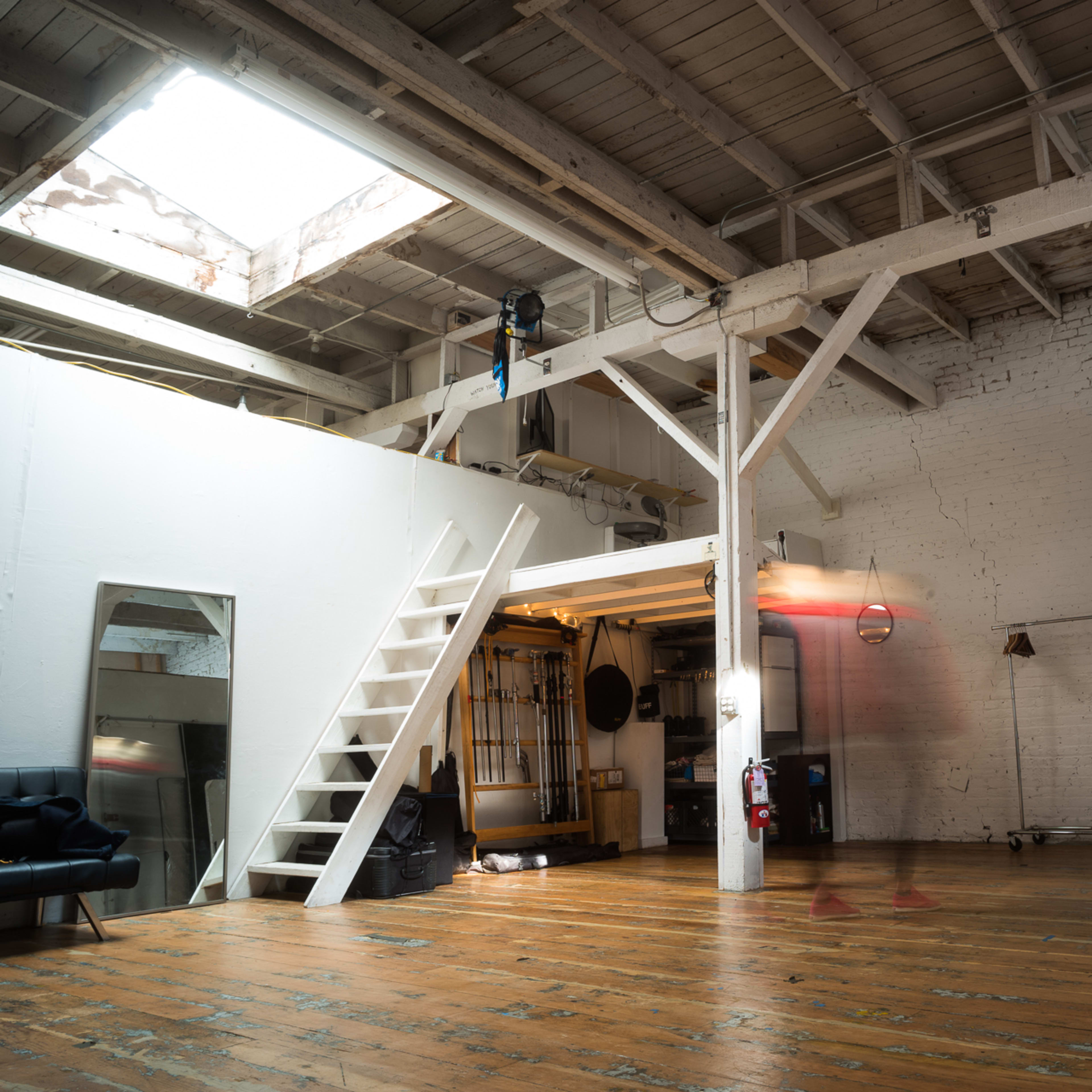 A spacious, industrial-style loft features wooden floors, exposed beams, and a staircase leading to a lofted area.