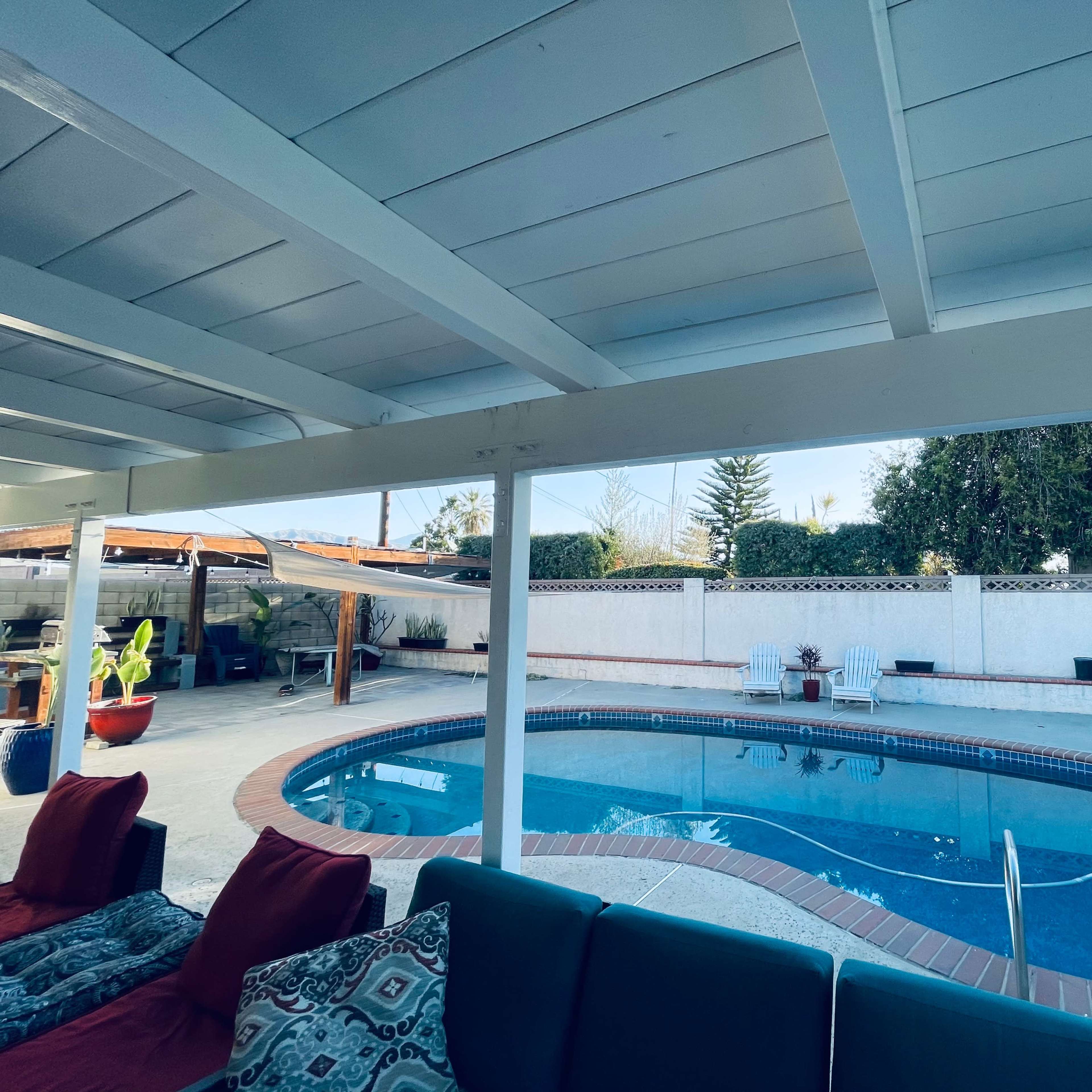 A backyard pool surrounded by a patio area with seating and potted plants.