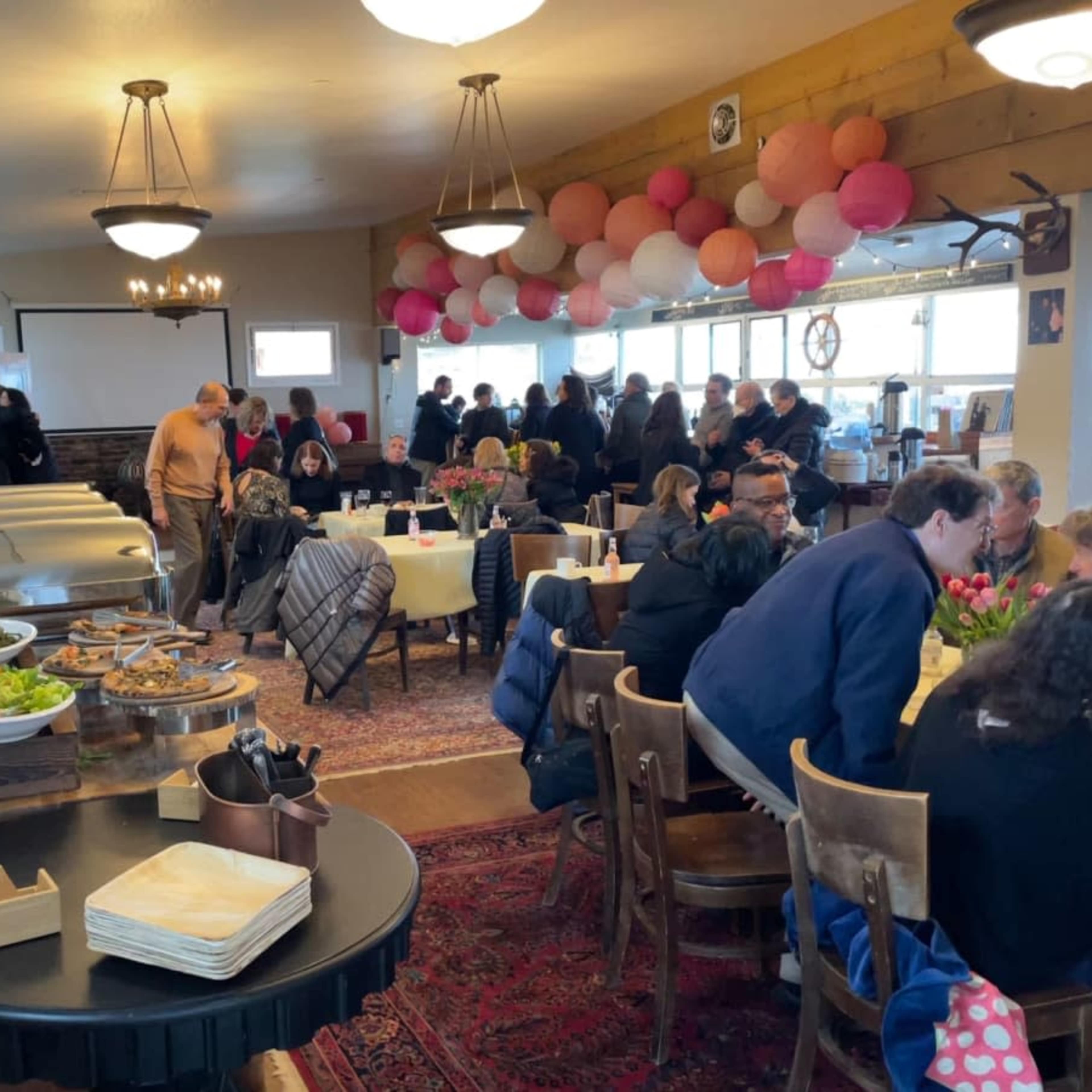 A bustling dining room with people gathered around tables, enjoying a meal, while a buffet station is set up in the foreground.