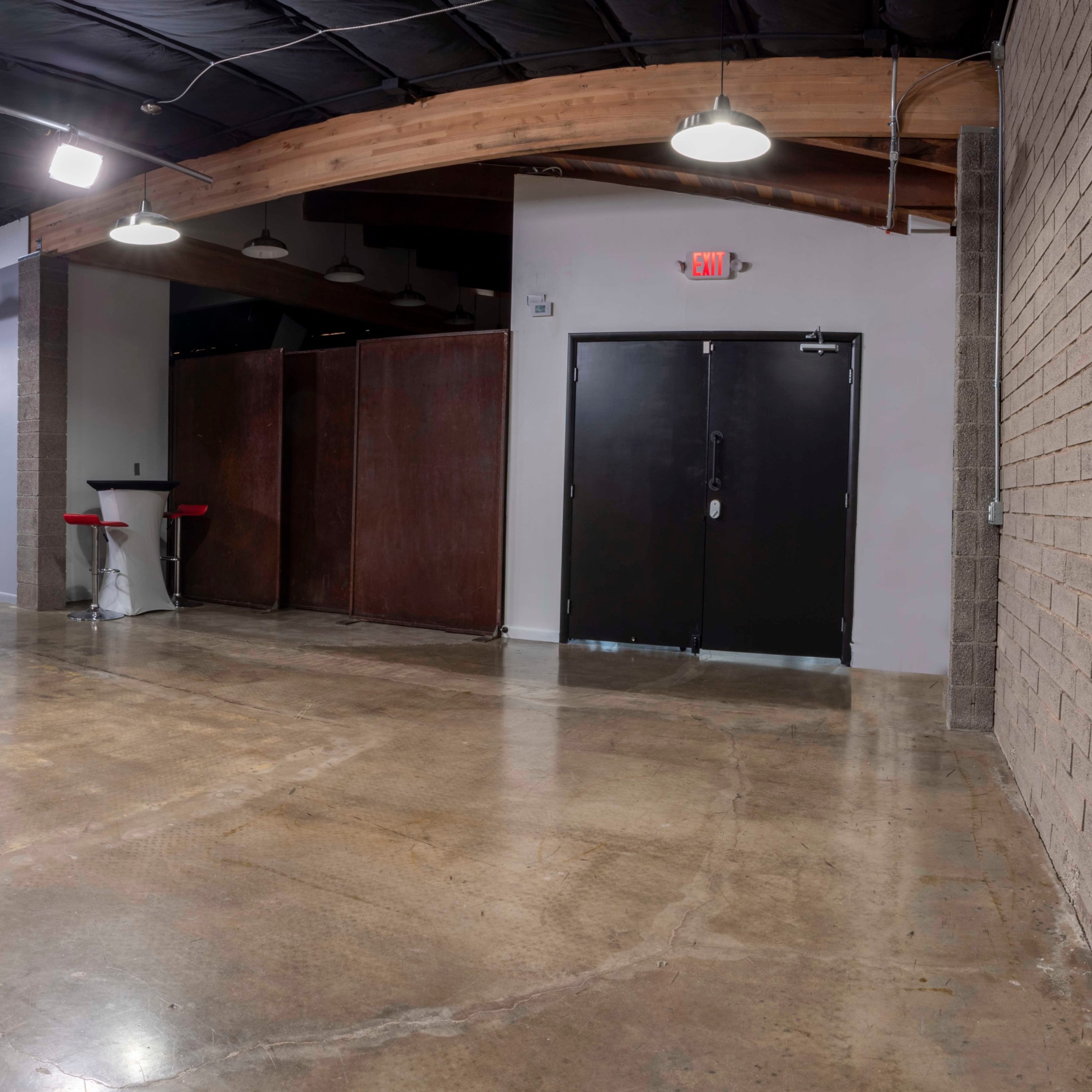 A spacious, industrial-style hallway with polished concrete floors, dim overhead lighting, and various areas for seating and entry.