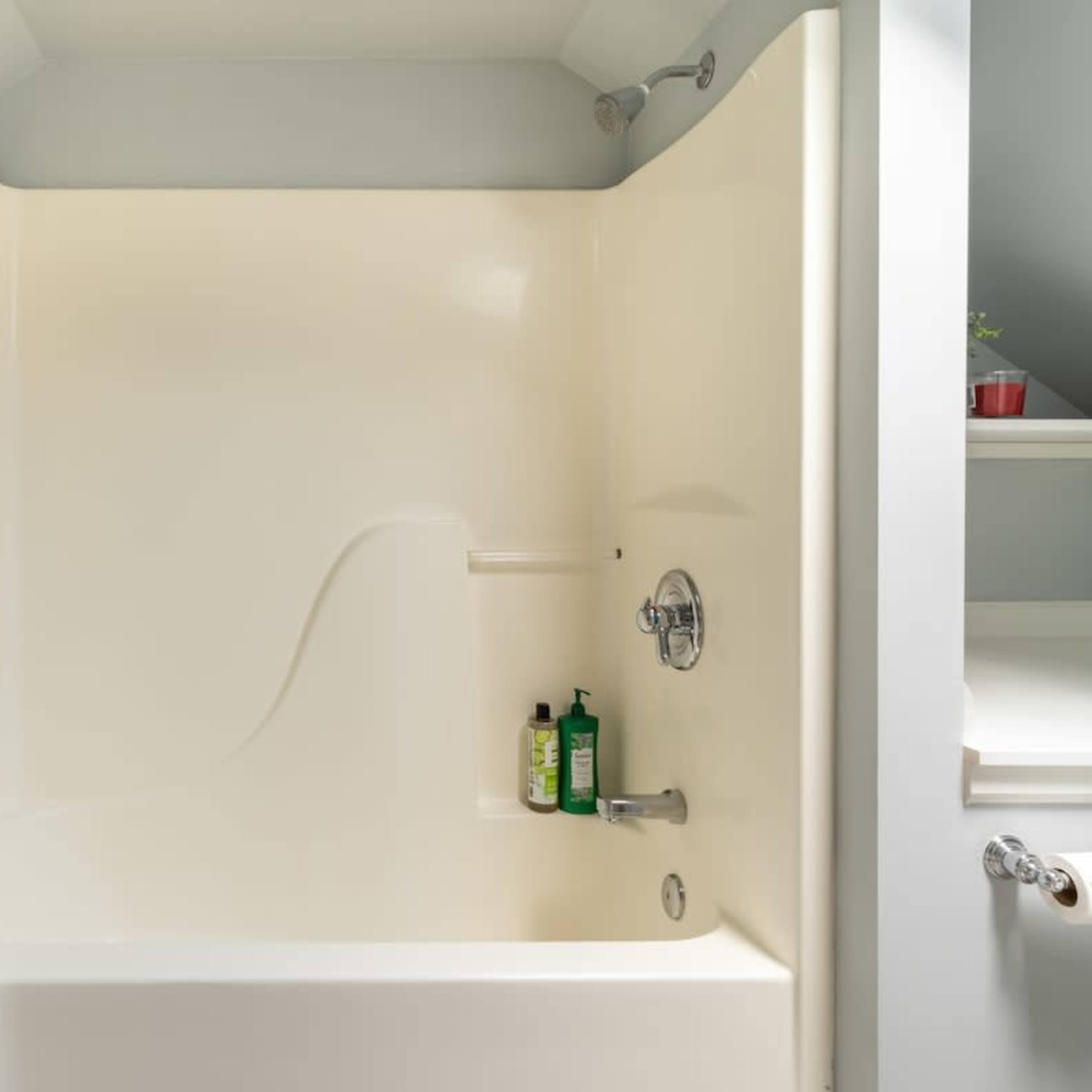A clean, empty bathtub and shower area with a shampoo bottle on the side.
