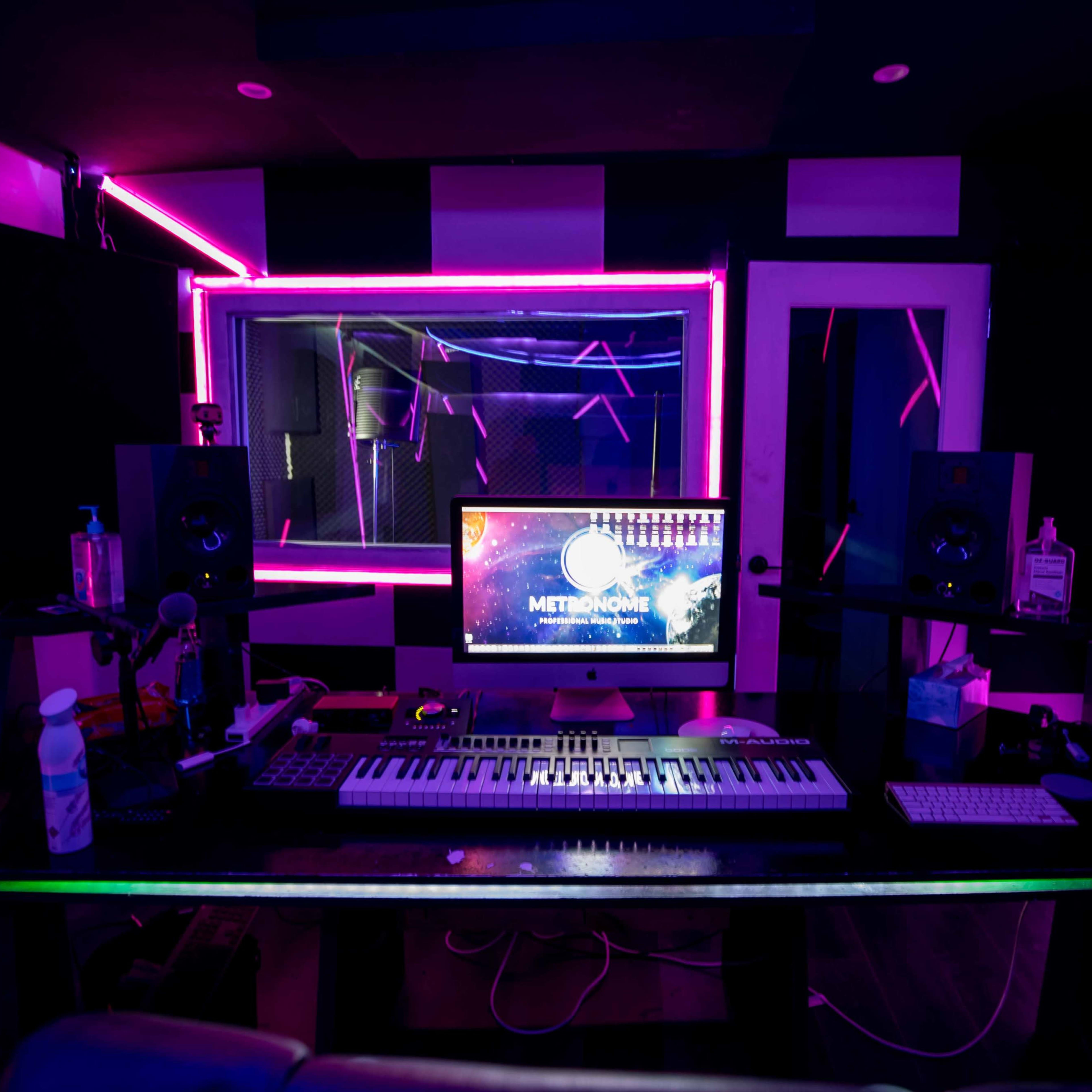 A modern music studio features a keyboard, speakers, and a computer monitor surrounded by colorful neon lighting.