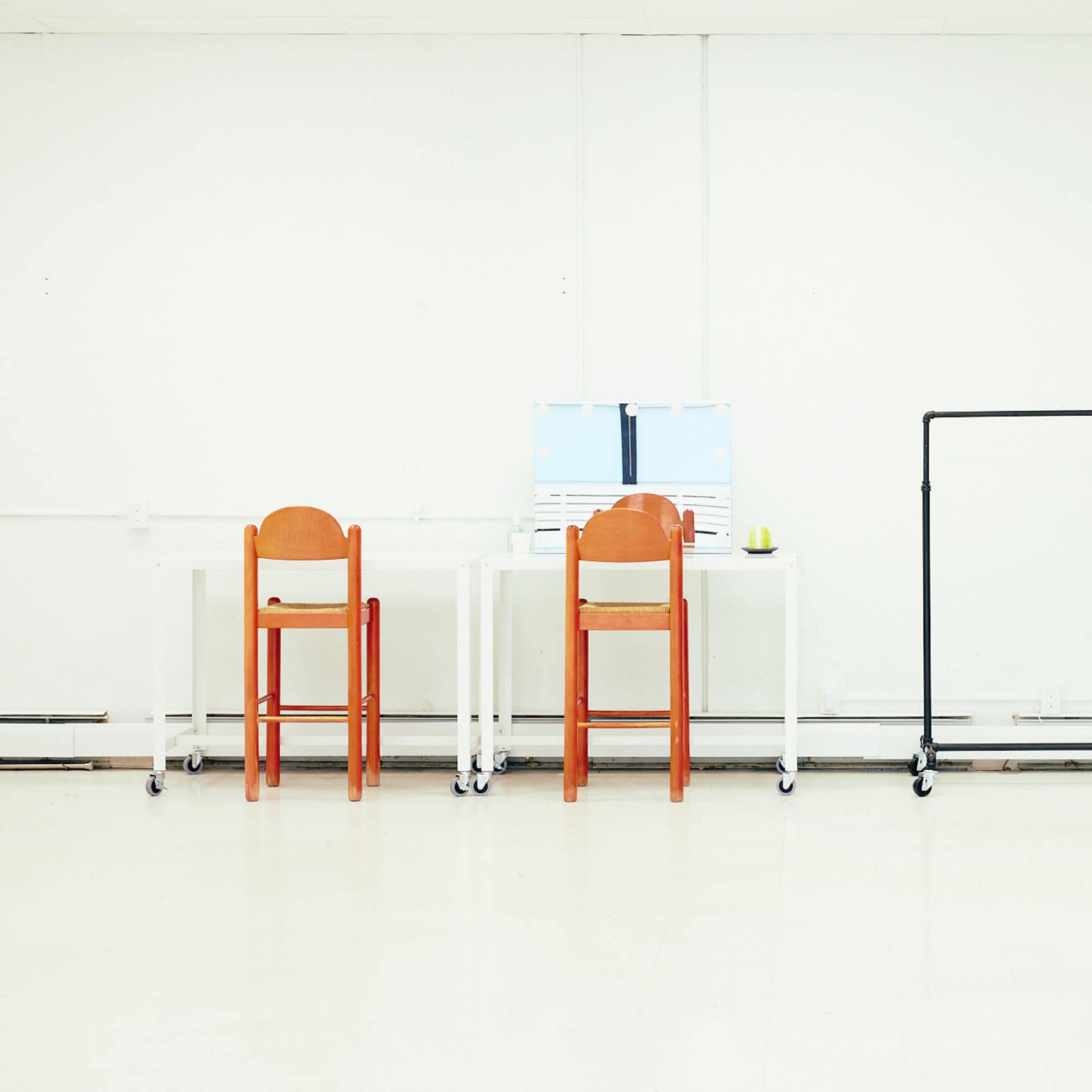 Three chairs, a desk, and two clothing racks positioned against a white wall in a spacious, well-lit room.