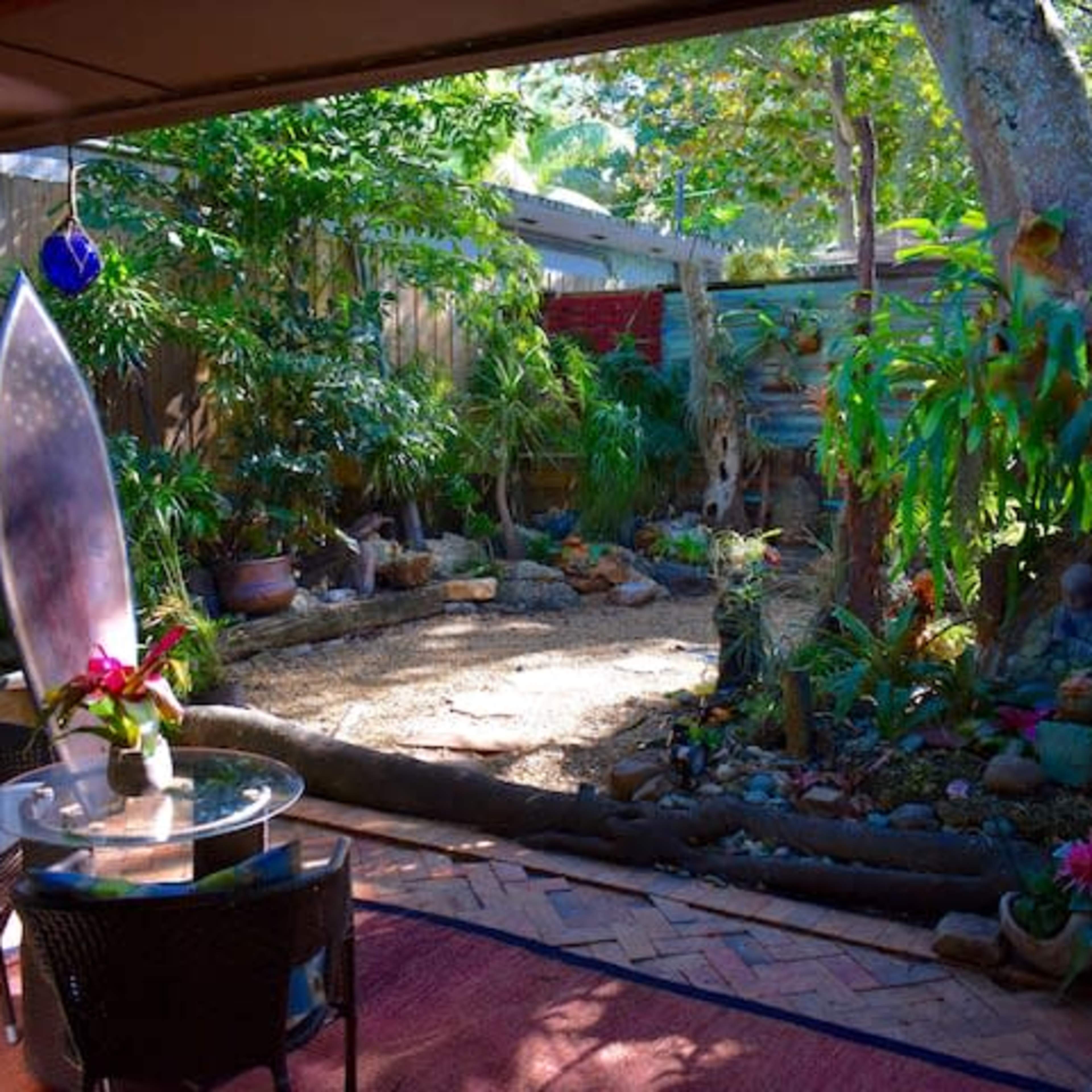 A small garden area is visible from a covered patio, featuring a sandy circular space surrounded by tropical plants and decorative stone elements.