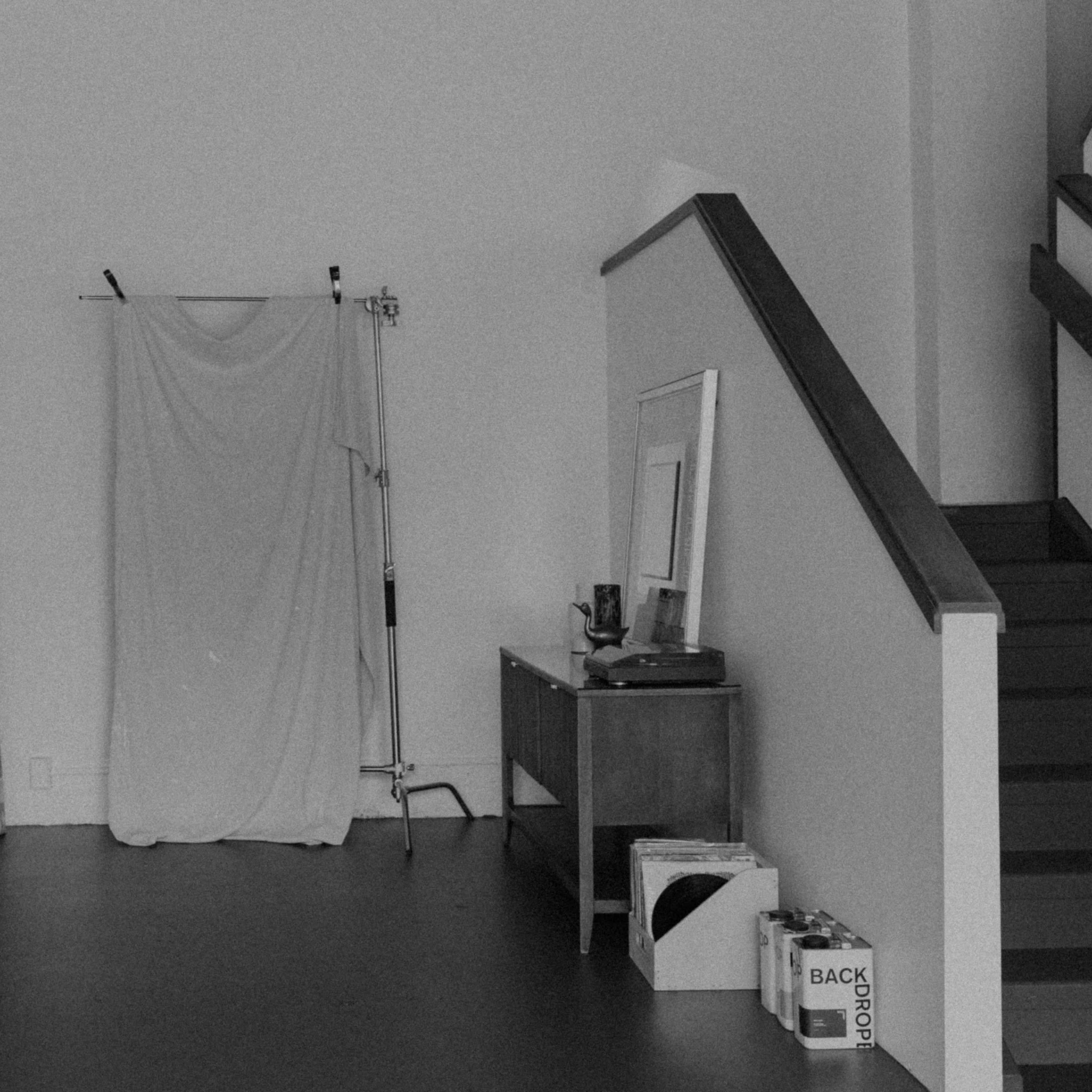 A minimalist room with a draped backdrop on a stand, a staircase, and various items including a mirror and boxes along the walls.
