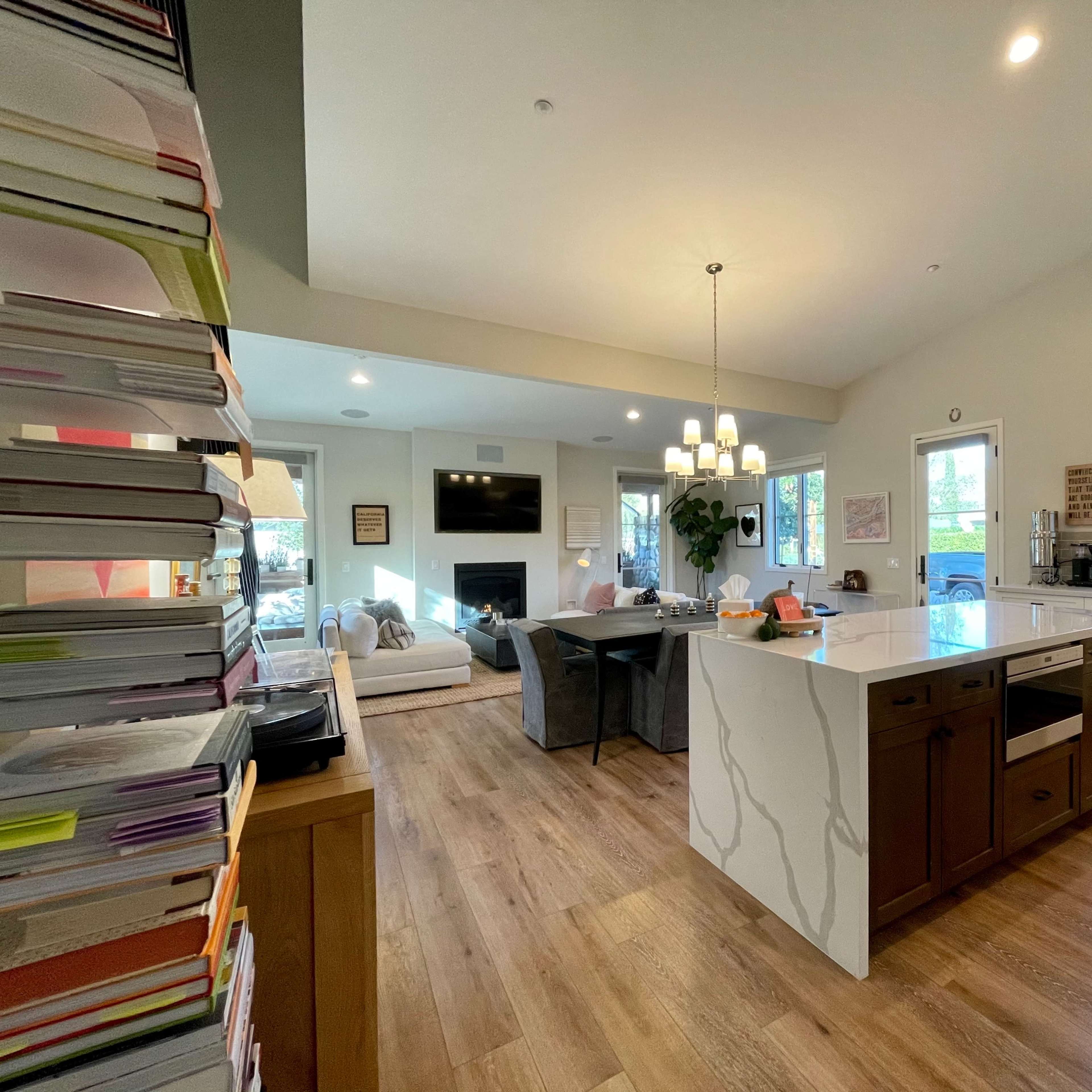 A modern kitchen and living area with light-colored cabinets, a large island, and a stack of papers on the left.