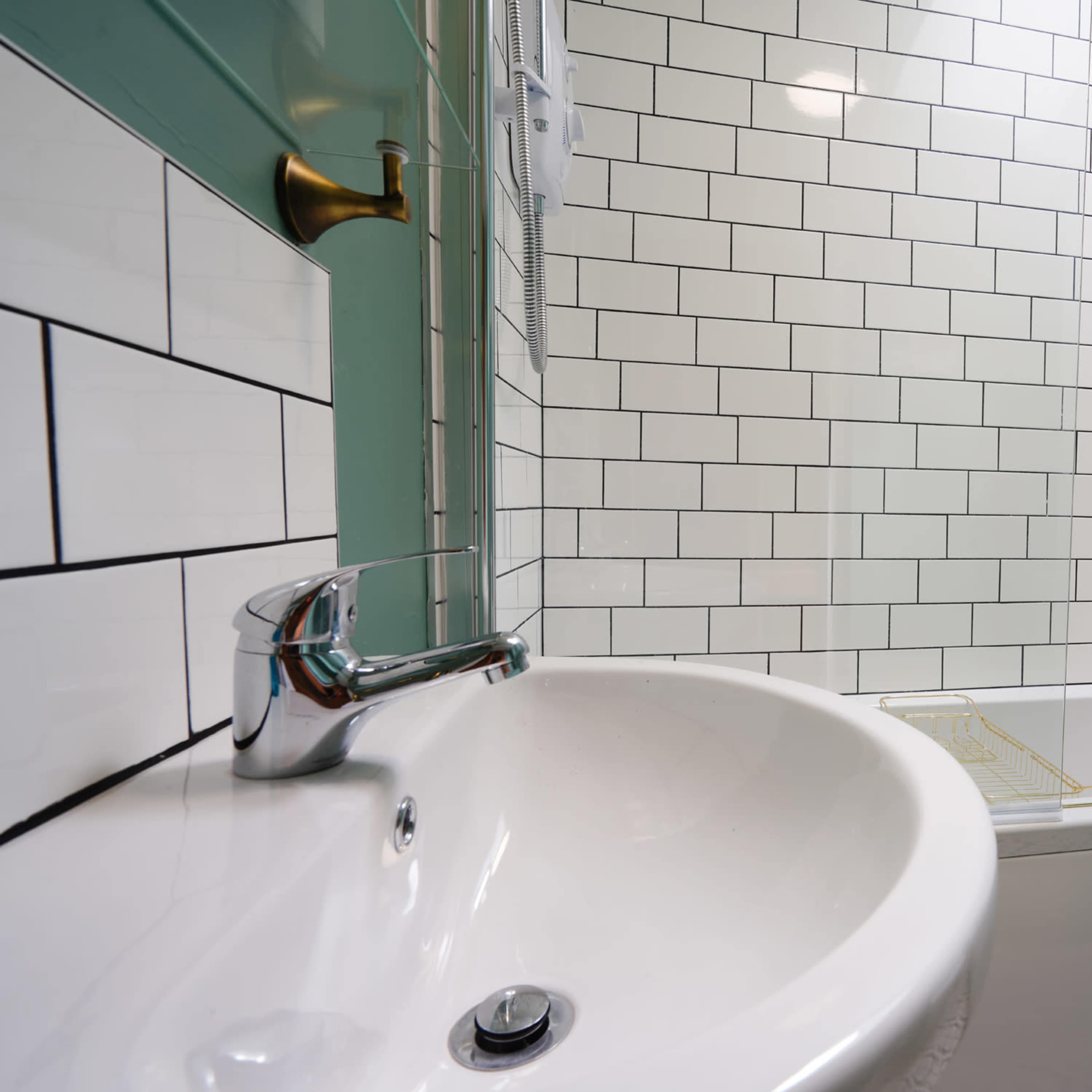 A bathroom with a white sink and a bathtub surrounded by white and green tiled walls.