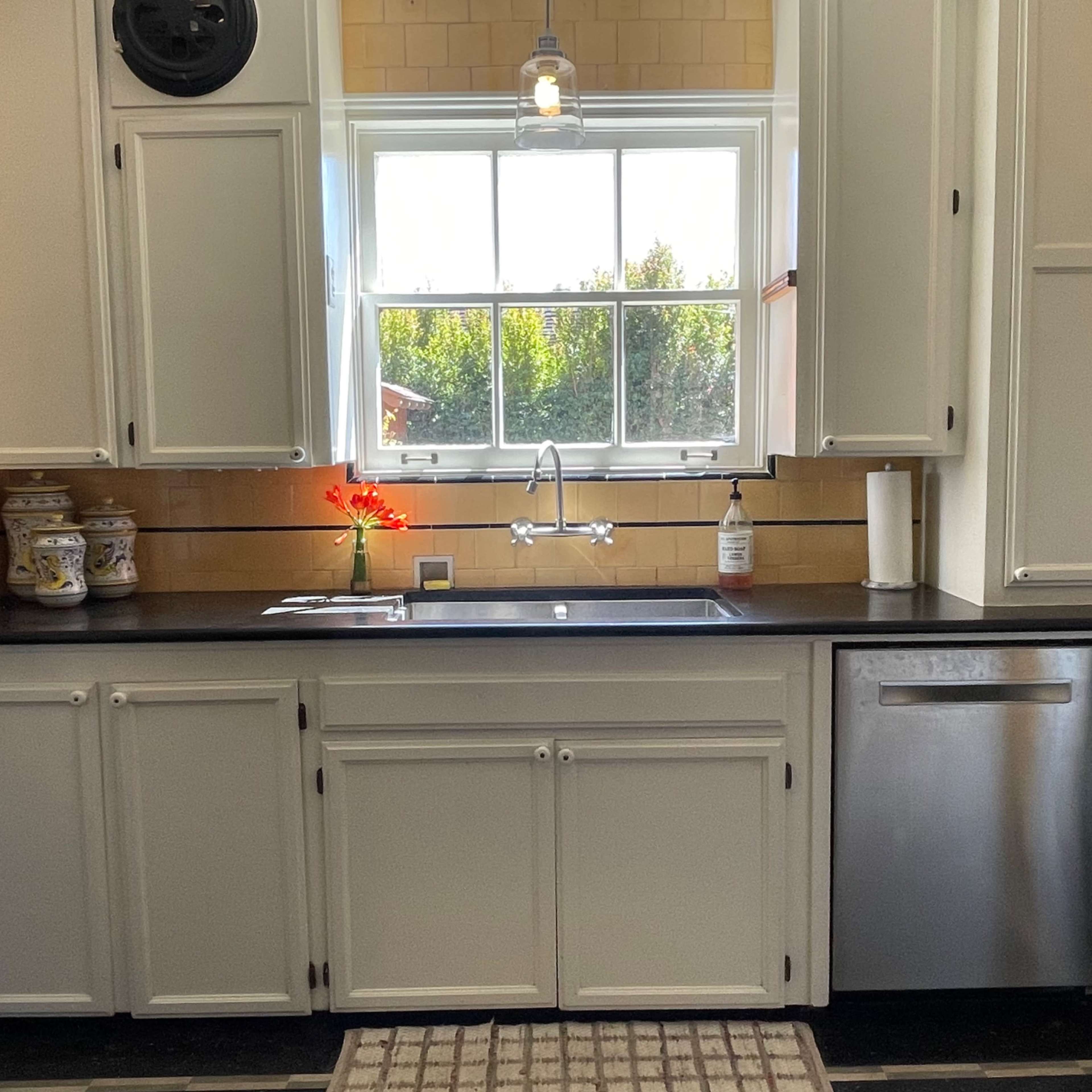 A kitchen with white cabinets, a black countertop, a window above the sink, and a dishwasher beside the sink.