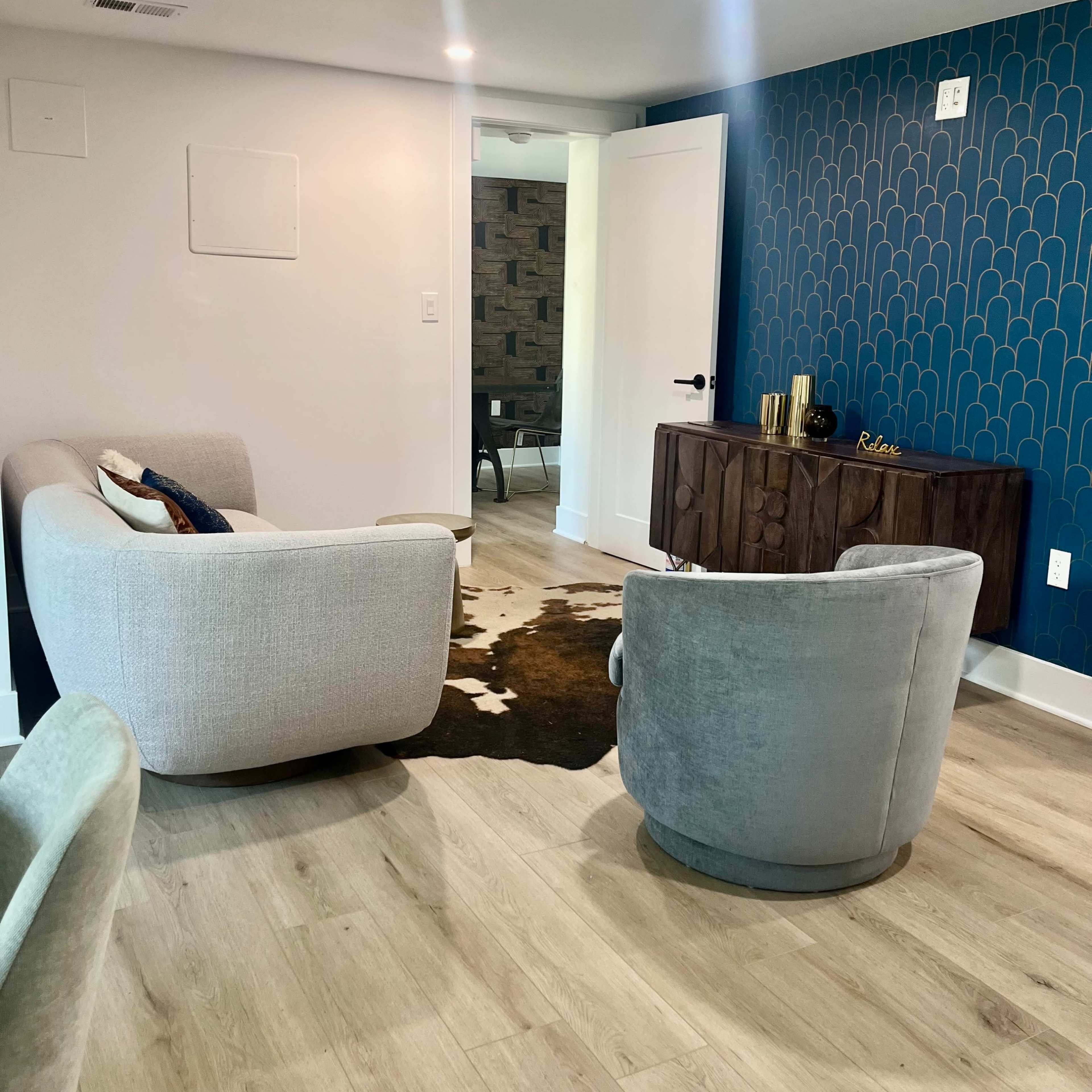 A modern living space featuring two upholstered chairs, a wall with a blue patterned design, and a wooden sideboard with decorative items.