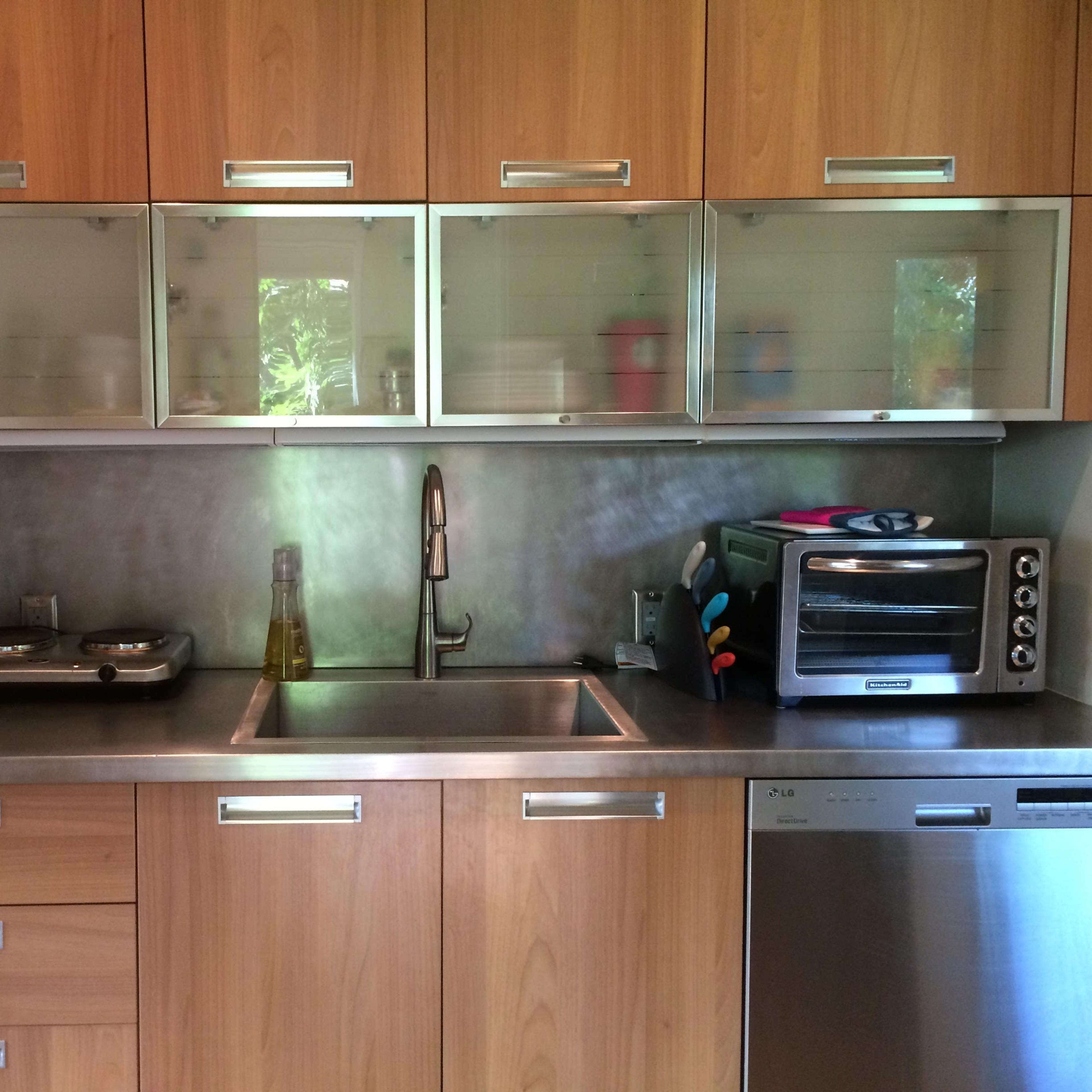 A modern kitchen with wooden cabinetry, a stainless steel sink, a gas stove, an oven, and various kitchen tools neatly arranged.