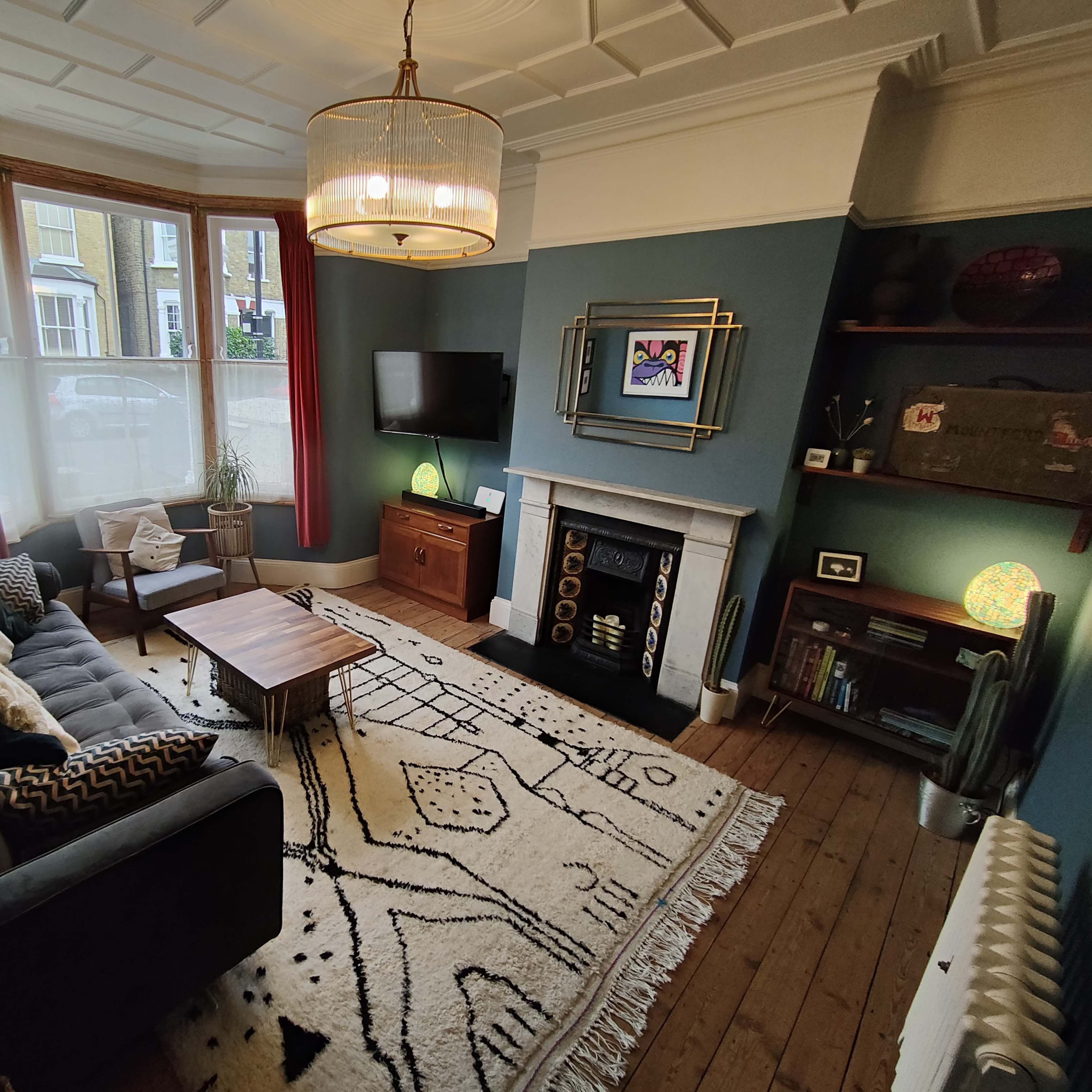 A stylish living room featuring a gray sofa, a wooden coffee table, a vintage fireplace, and a television mounted on the wall.