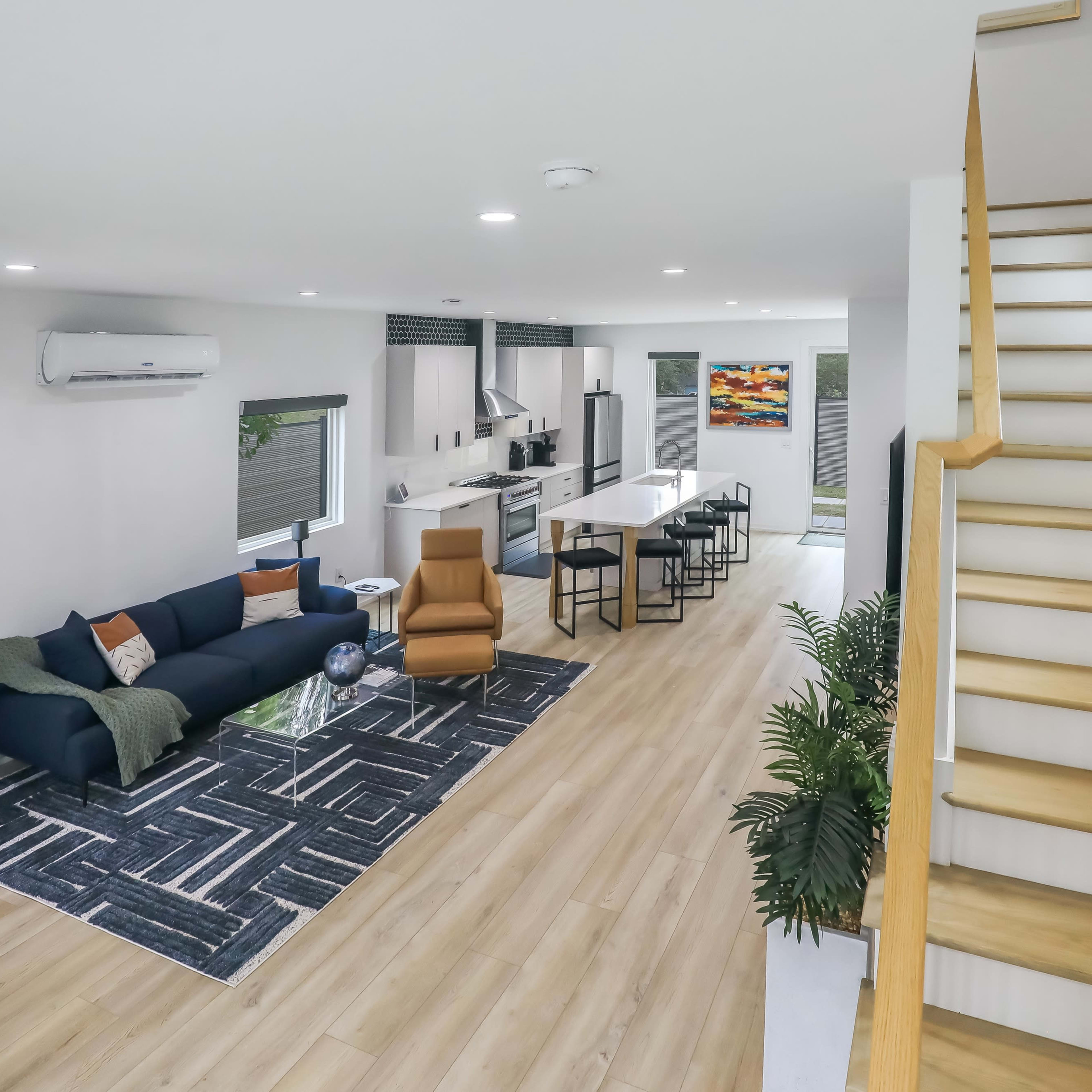 A modern open-concept living space with a sofa, dining area, and staircase leading to the upper level.