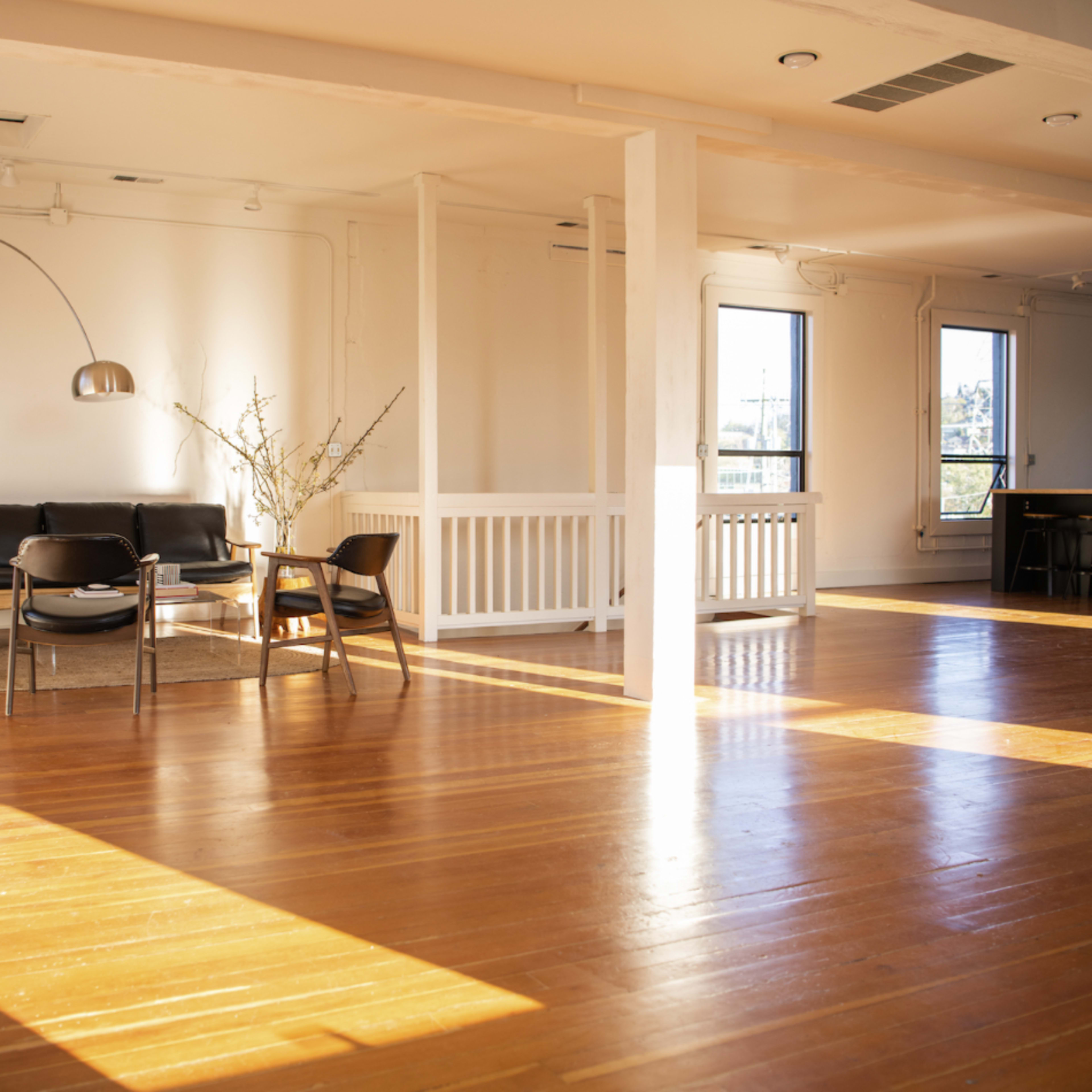 A bright, open room with wooden floors, a black sofa, and a modern arc floor lamp, alongside a potted plant and a small table.
