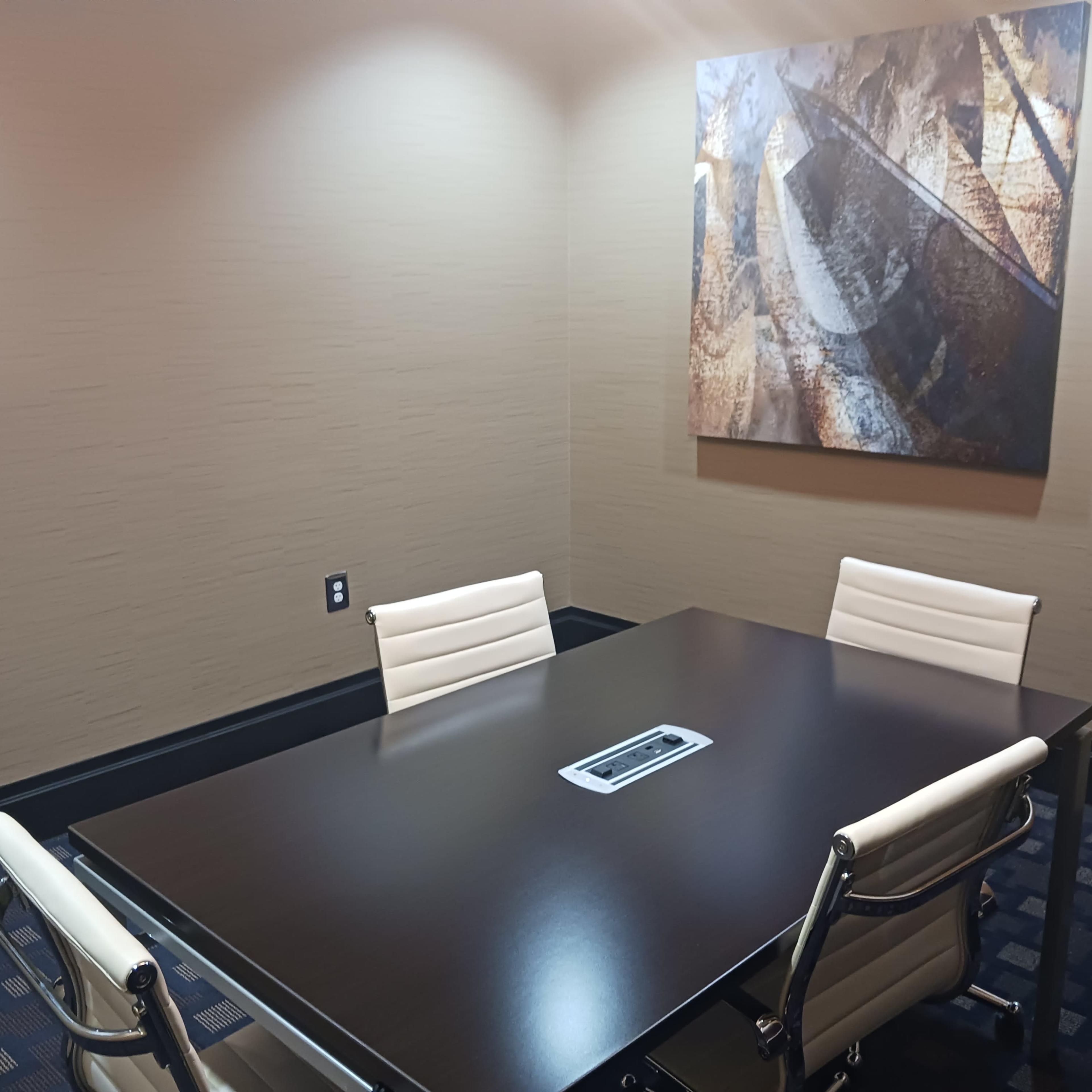 A small conference room with a dark wooden table and four white chairs, accompanied by a large abstract painting on the wall.