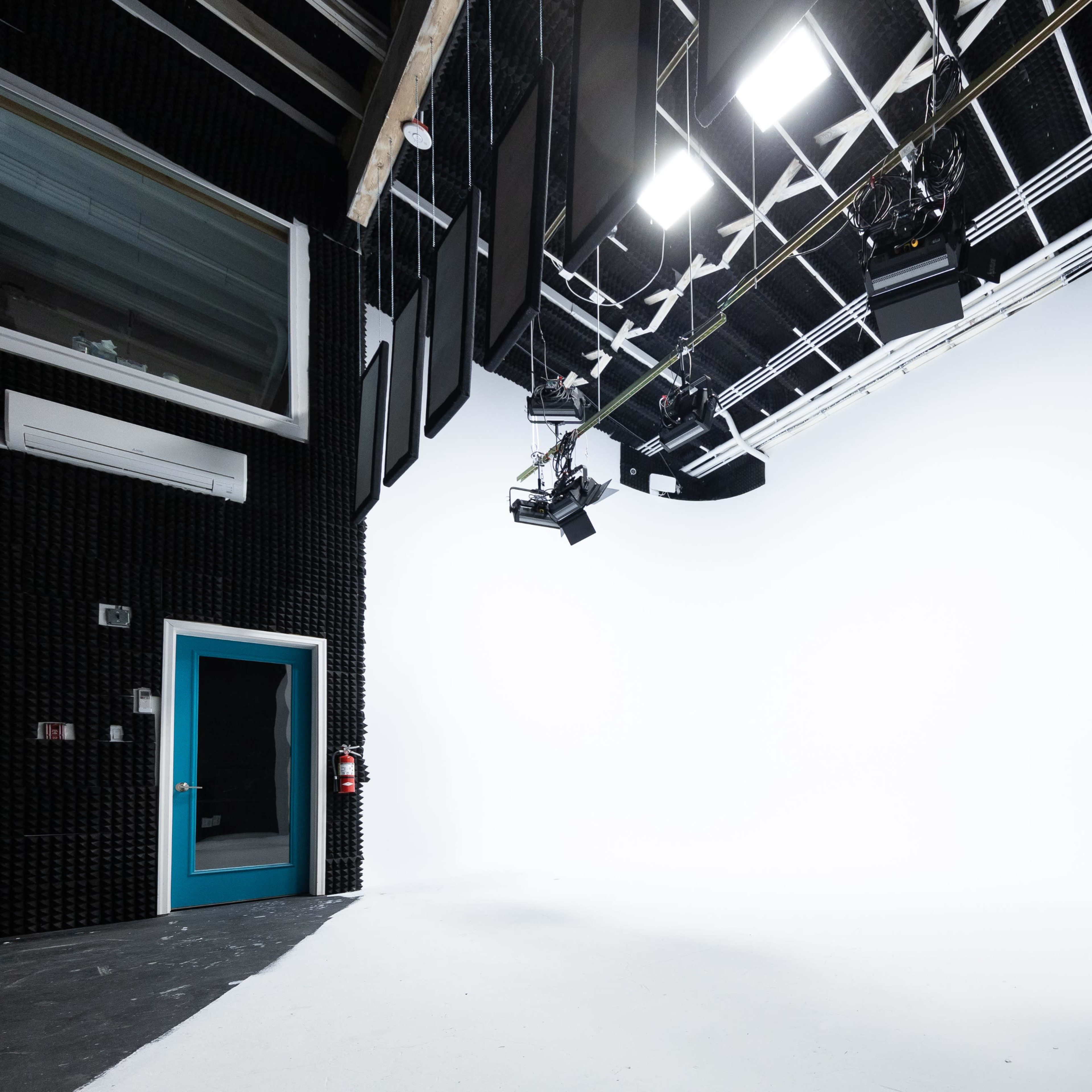A spacious, empty studio with a white backdrop, studio lights, and soundproofing panels on the walls.