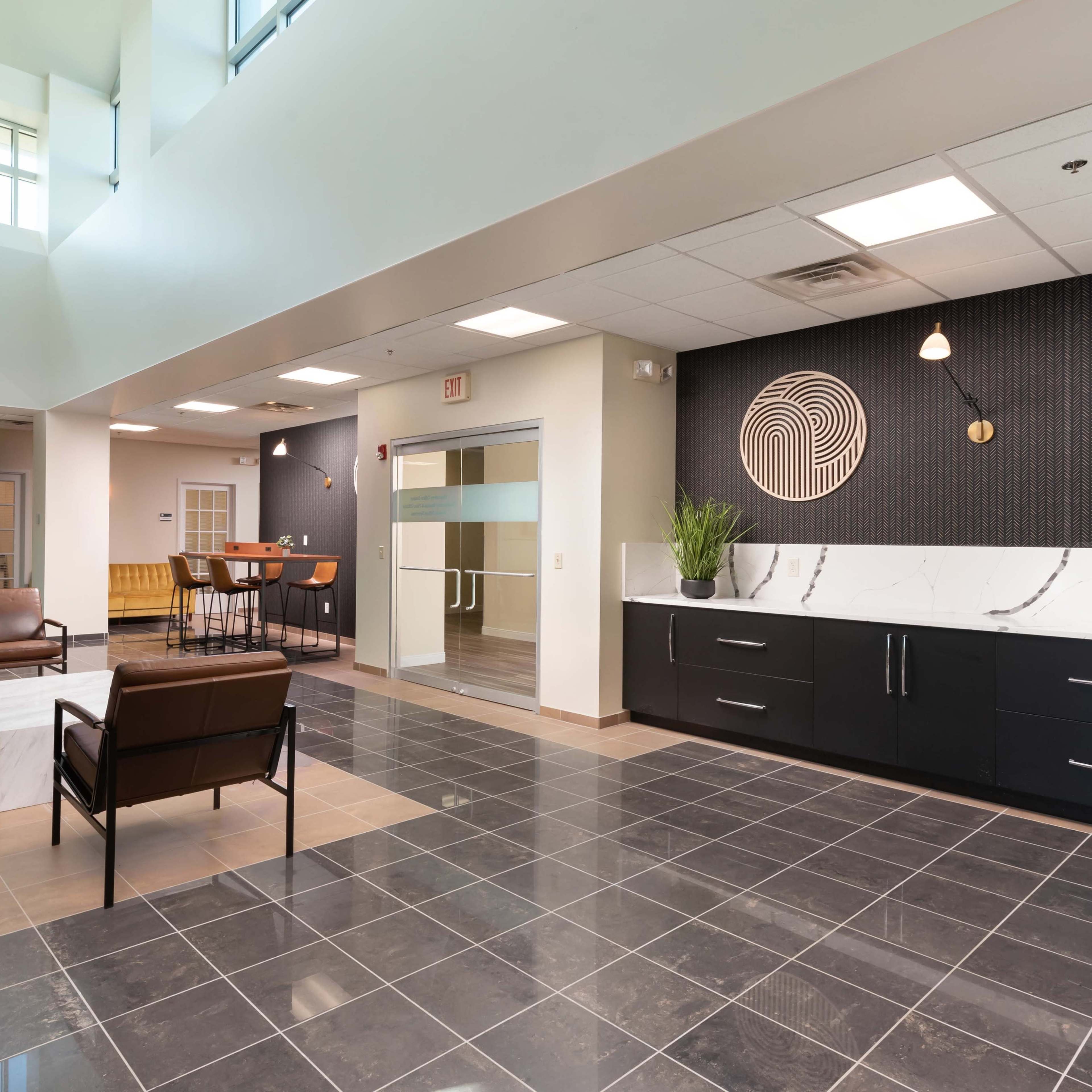 A modern lobby area featuring tiled flooring, contemporary furniture, and a reception area with a textured wall design.