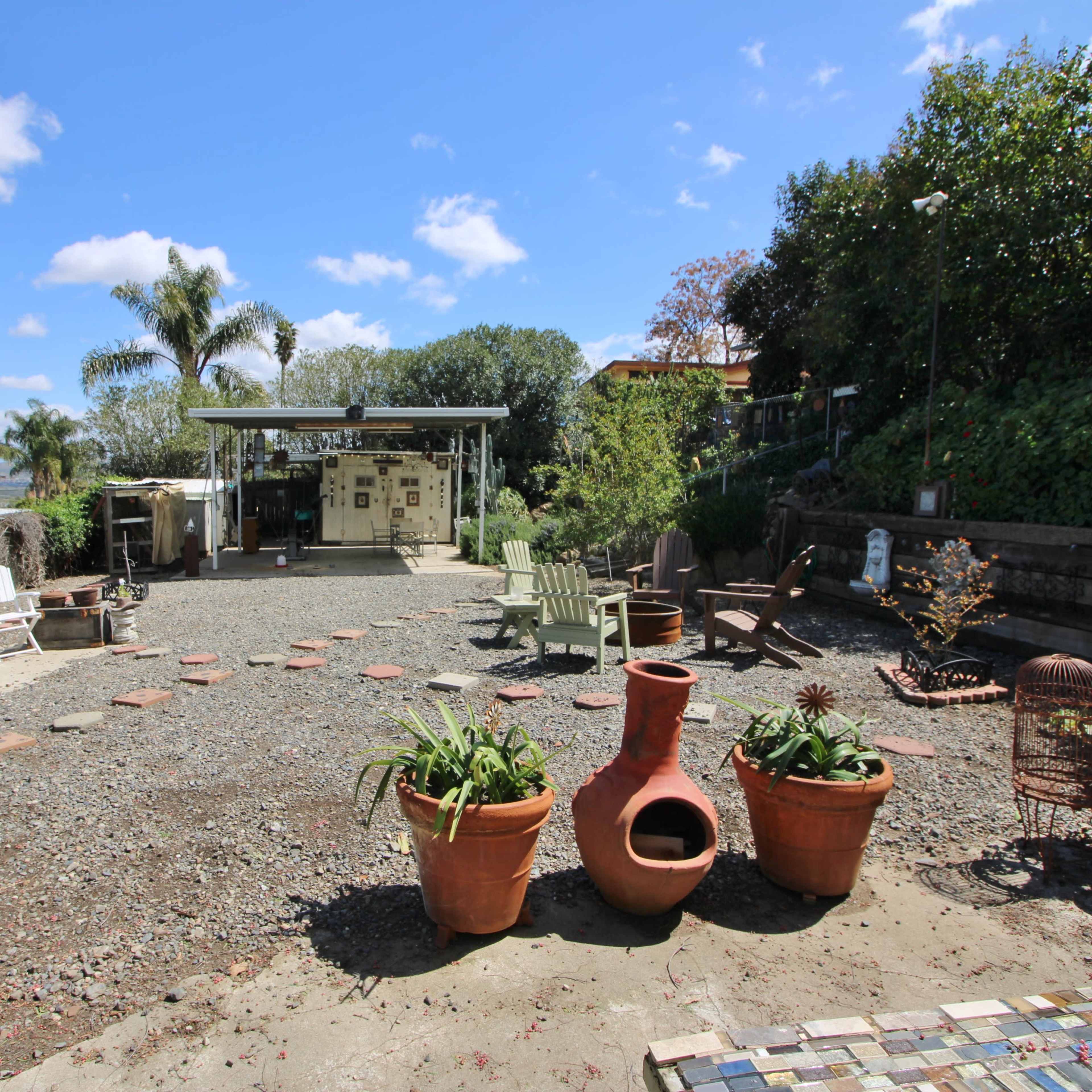 An outdoor area featuring various seating arrangements, potted plants, and a structure in the background under a clear blue sky.