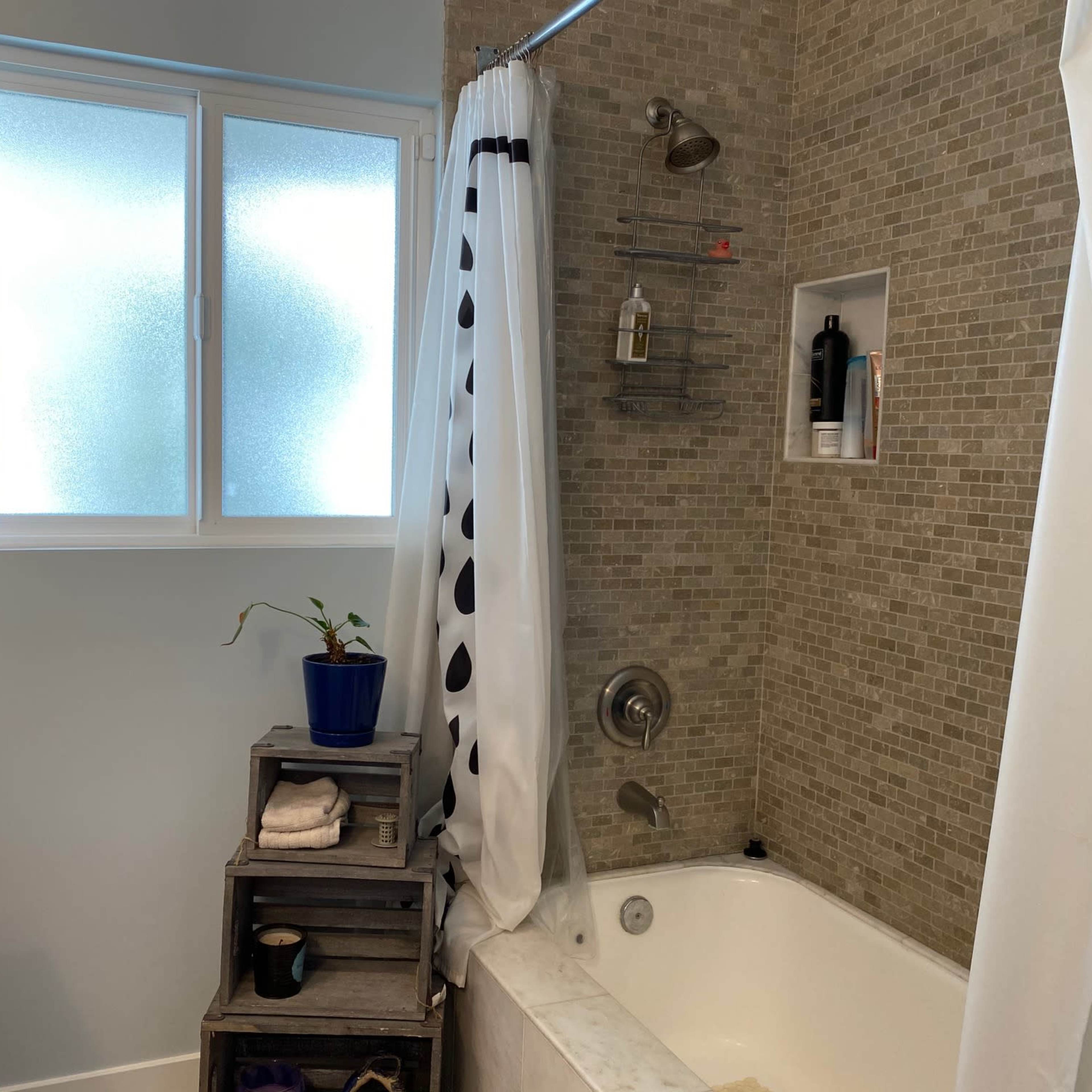 A bathroom with a bathtub, a shower curtain, a window, and a wooden crate holding toiletries.
