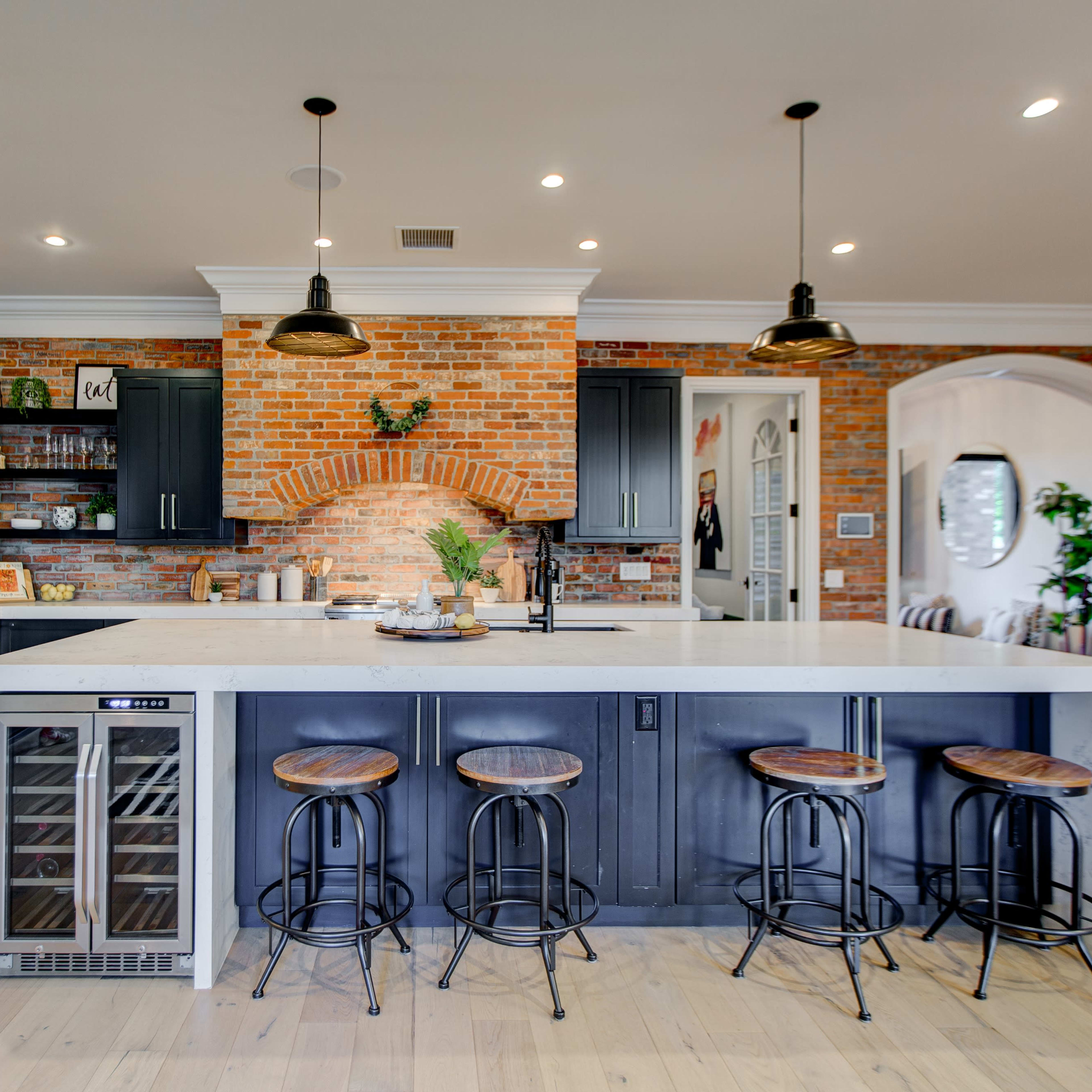 The kitchen features a large island with seating, black cabinetry, a brick arch, and modern lighting fixtures.