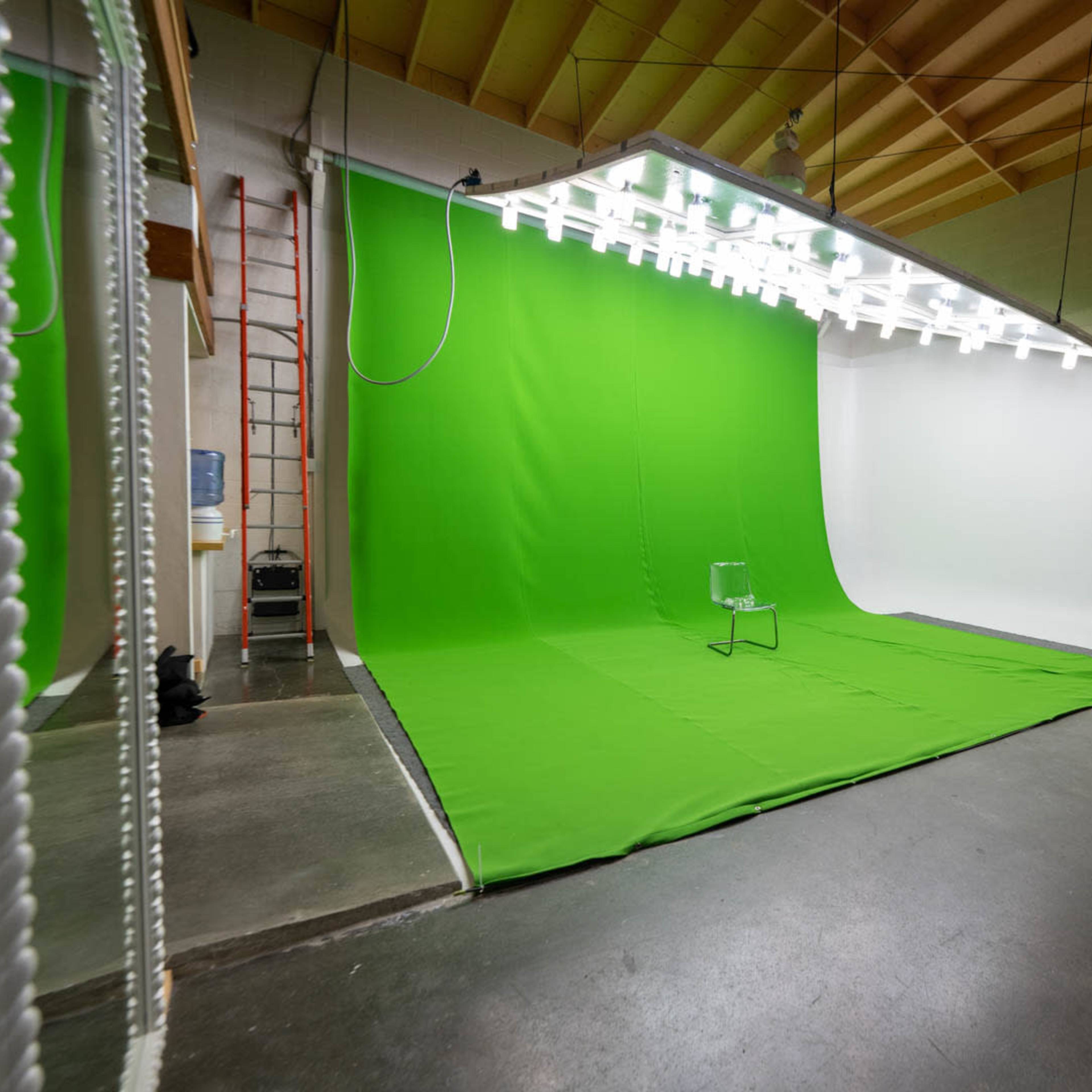 A photography studio with a green backdrop on one side and a white backdrop on the other, along with lighting and equipment arranged in the space.