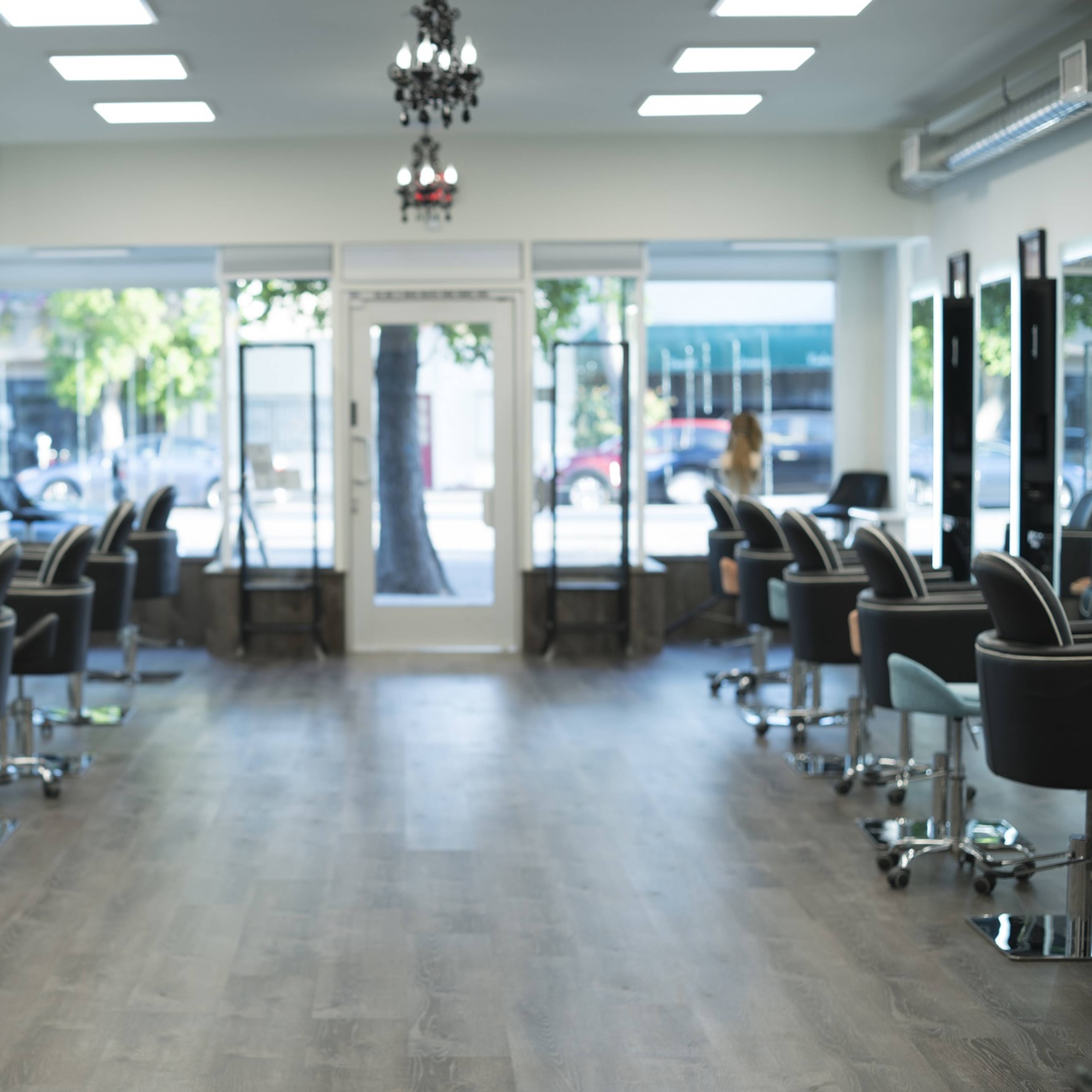 The interior of a modern salon with multiple salon chairs arranged in a row and large mirrors reflecting the space.