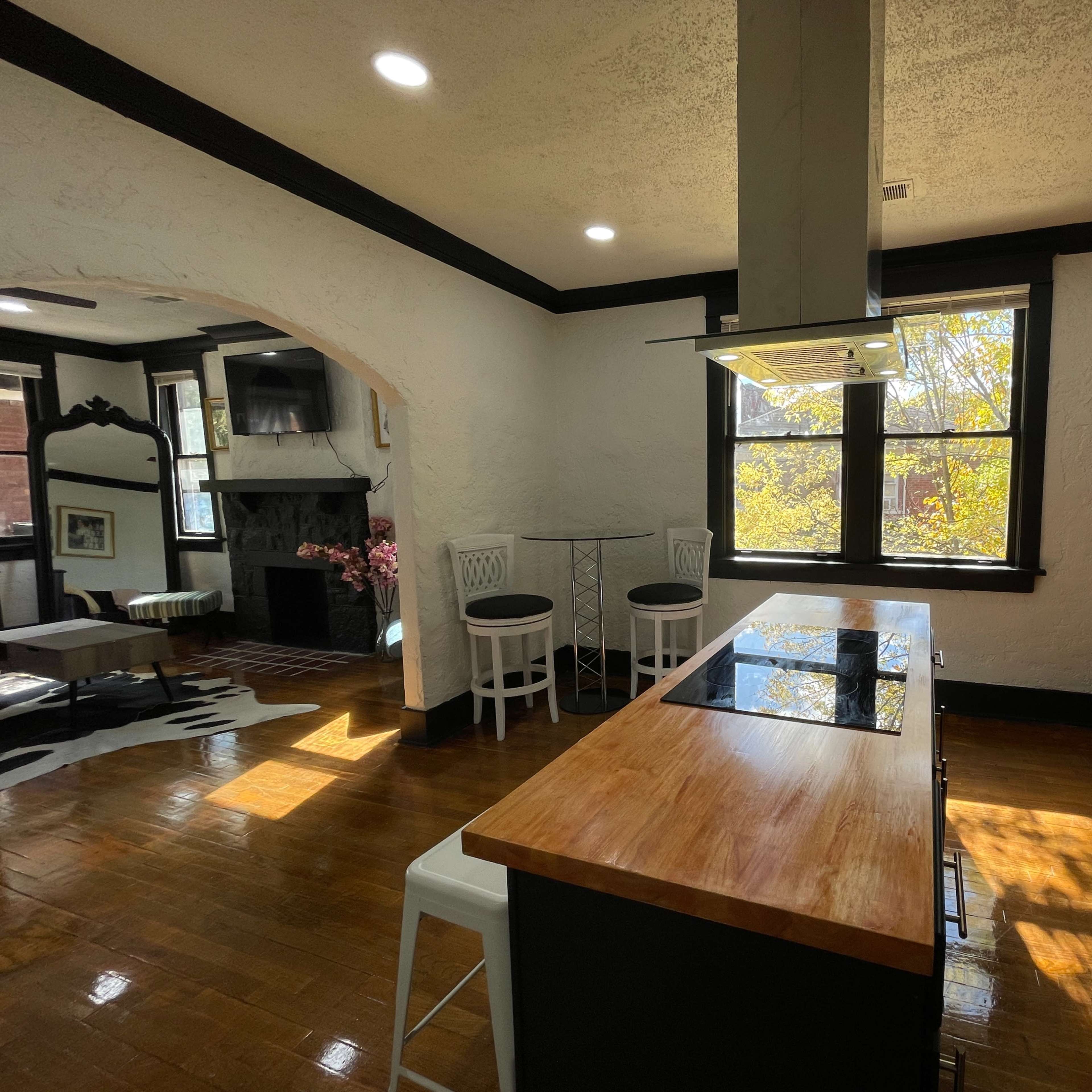The kitchen features a central island with a cooking surface, modern appliances, and wooden countertops, with a seating area and large windows allowing natural light.