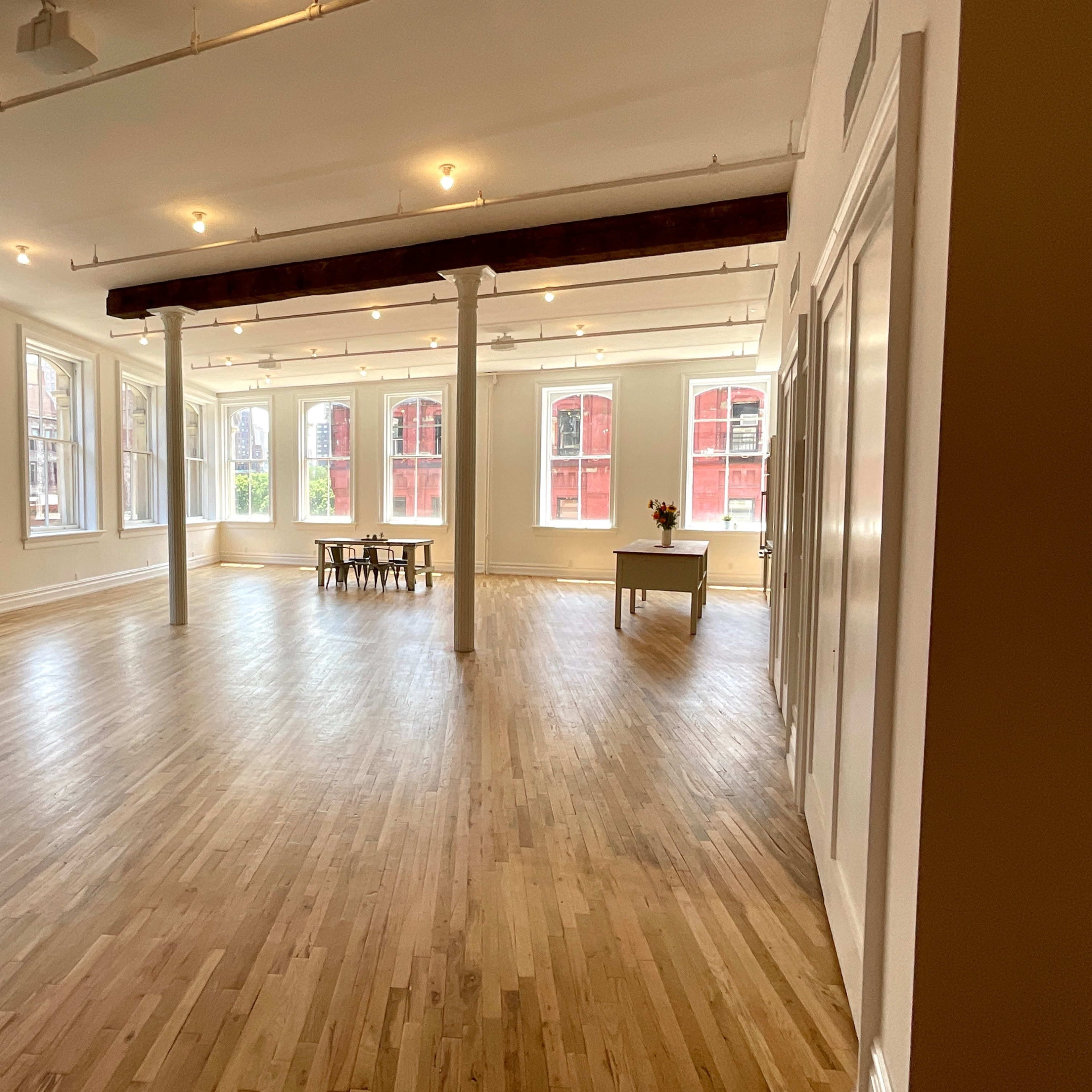 A bright, spacious room with large windows, hardwood flooring, and minimal furnishings including a sofa and a table.