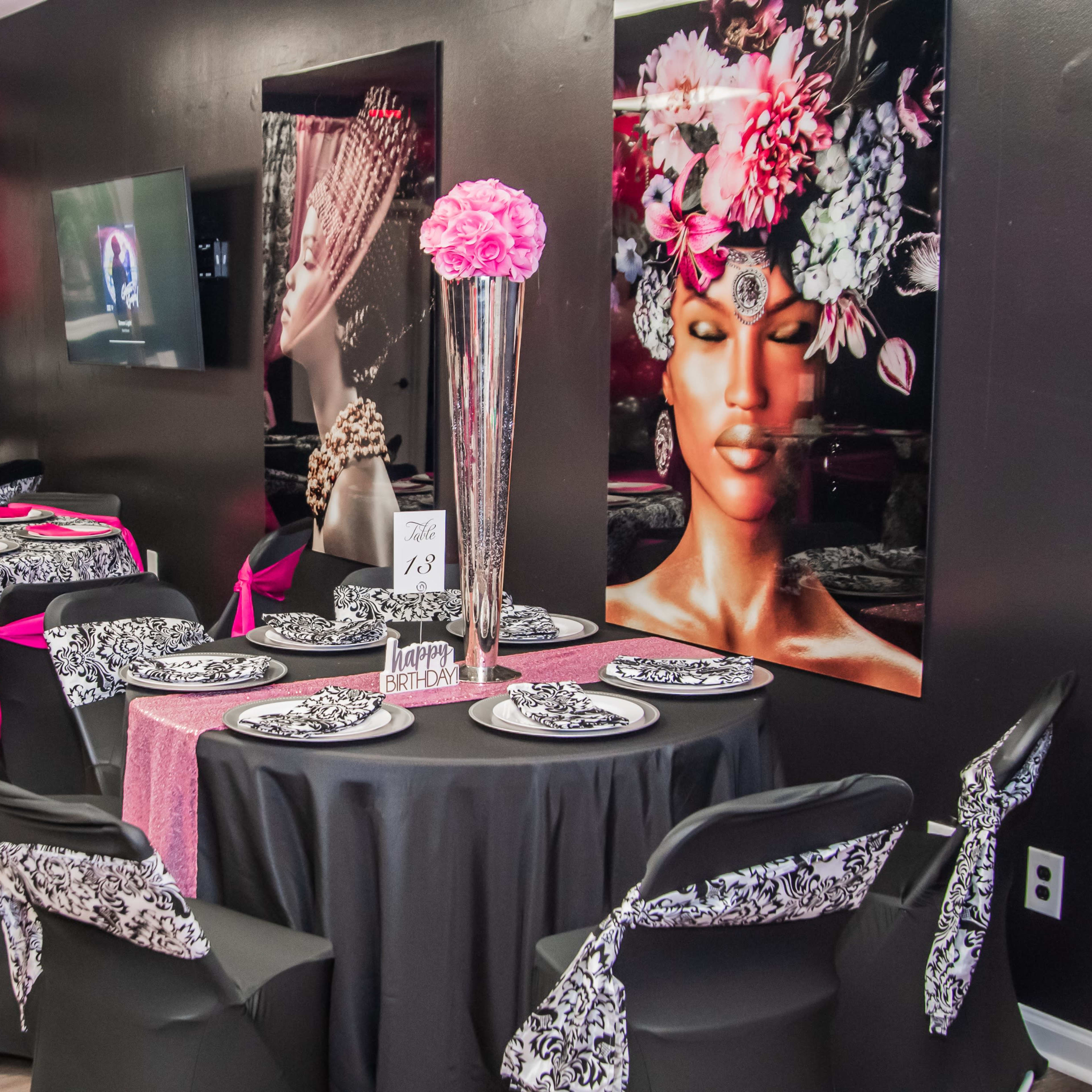A stylish event space featuring tables with black and pink table settings, adorned with floral centerpieces and decorative balloons.
