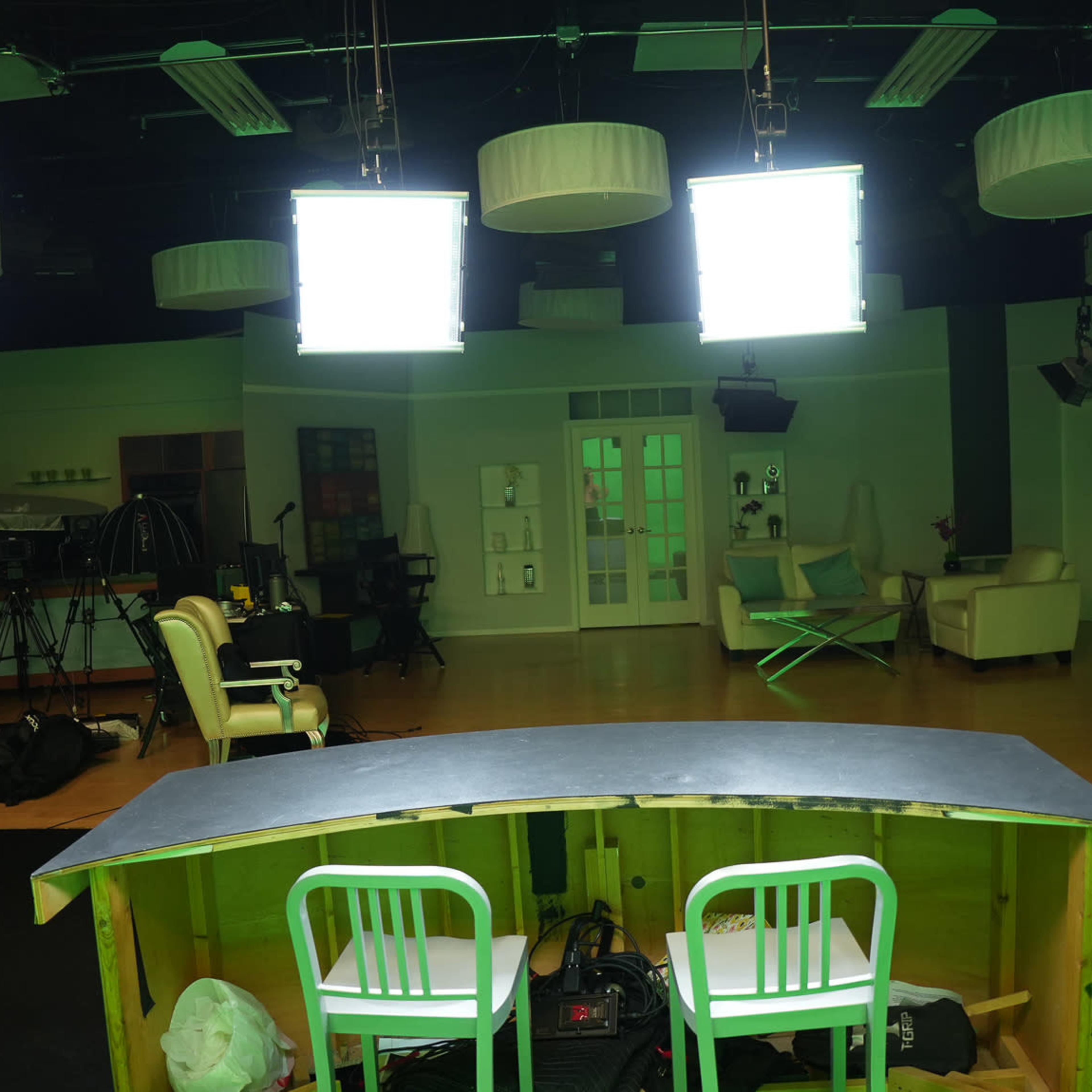 A television studio setup with bright overhead lights, a green screen area, and a counter with two chairs facing an empty space.