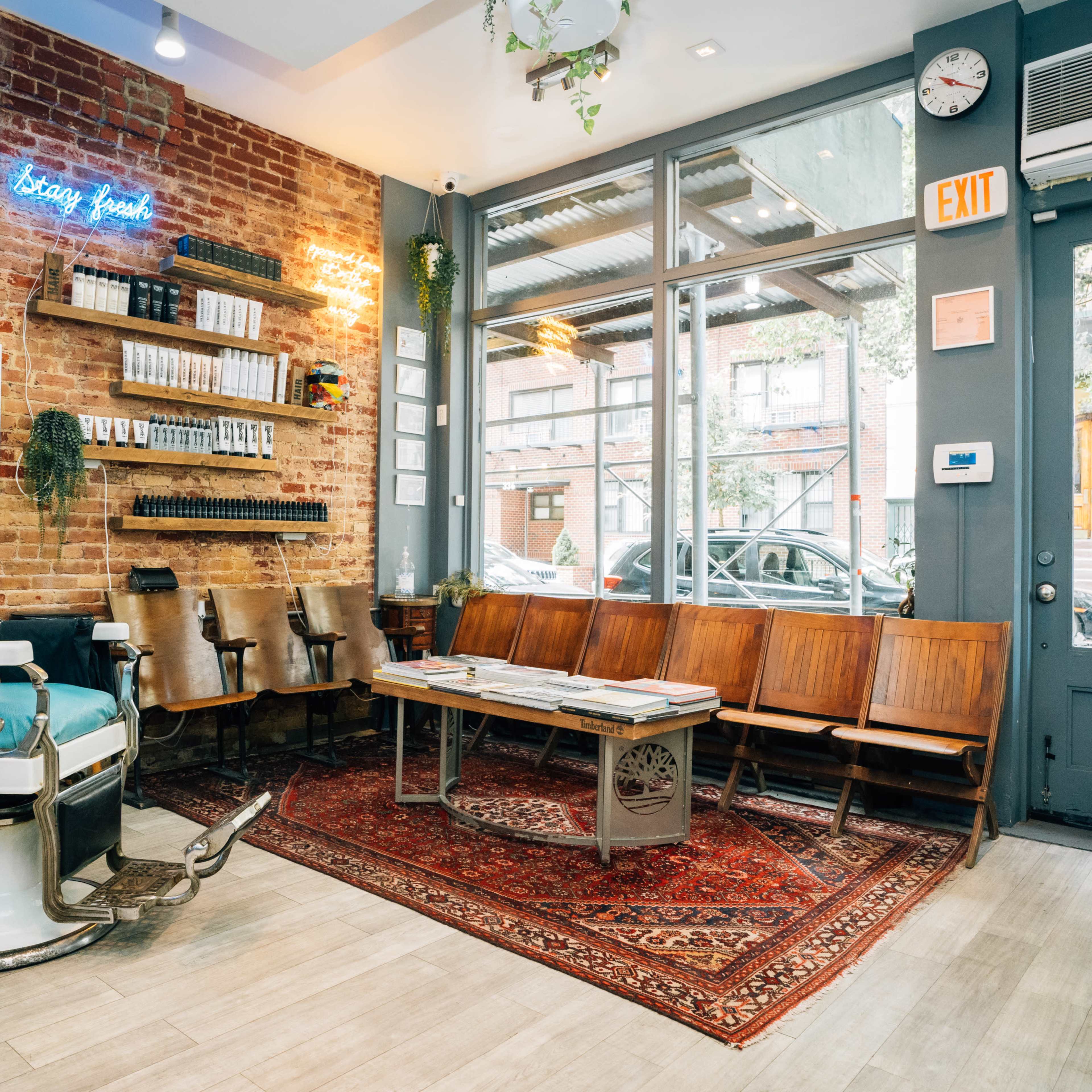 A barbershop interior with brick walls, vintage seating, a barber chair, and large windows letting in natural light.
