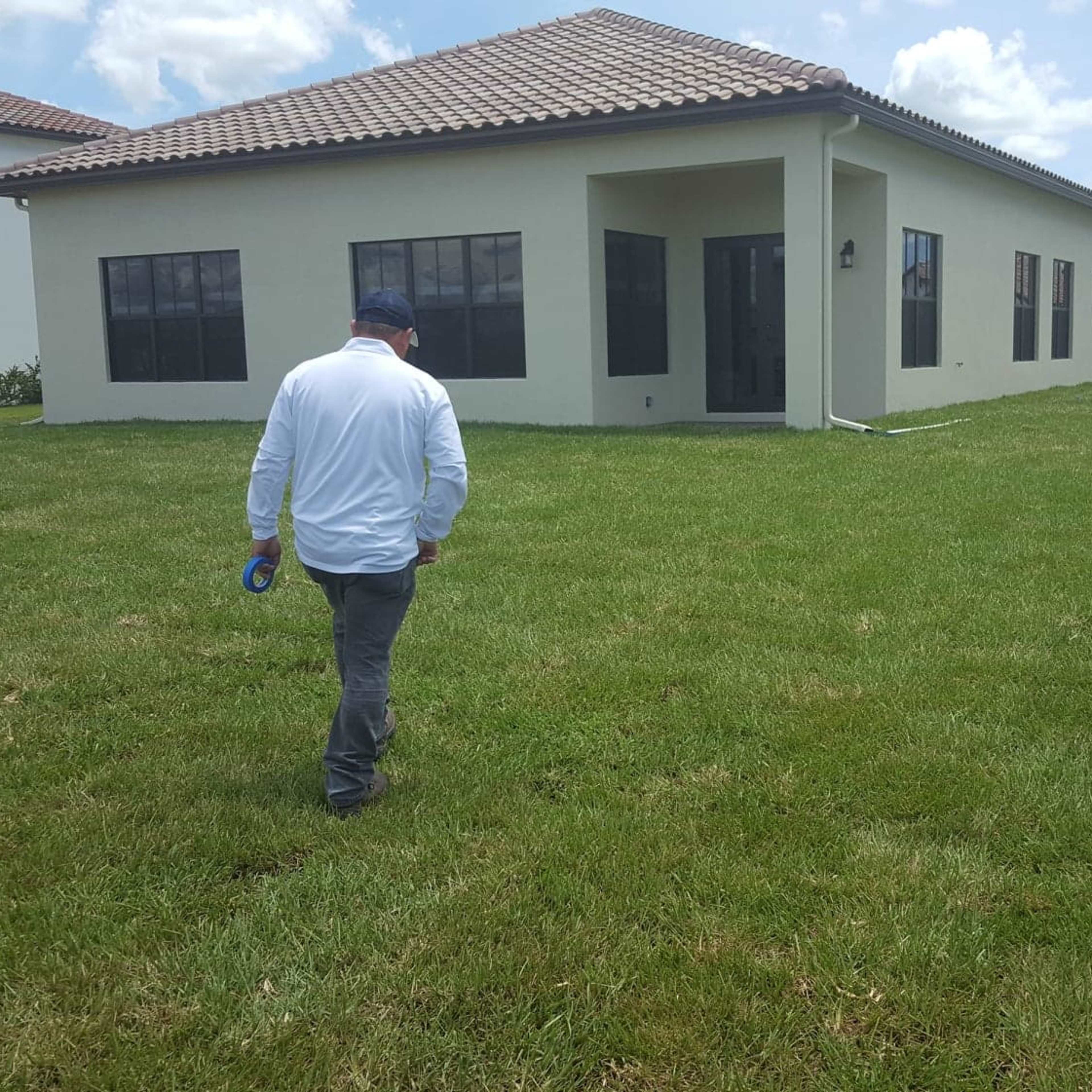 A person walks across a green lawn towards a large house with a flat roof and multiple windows.