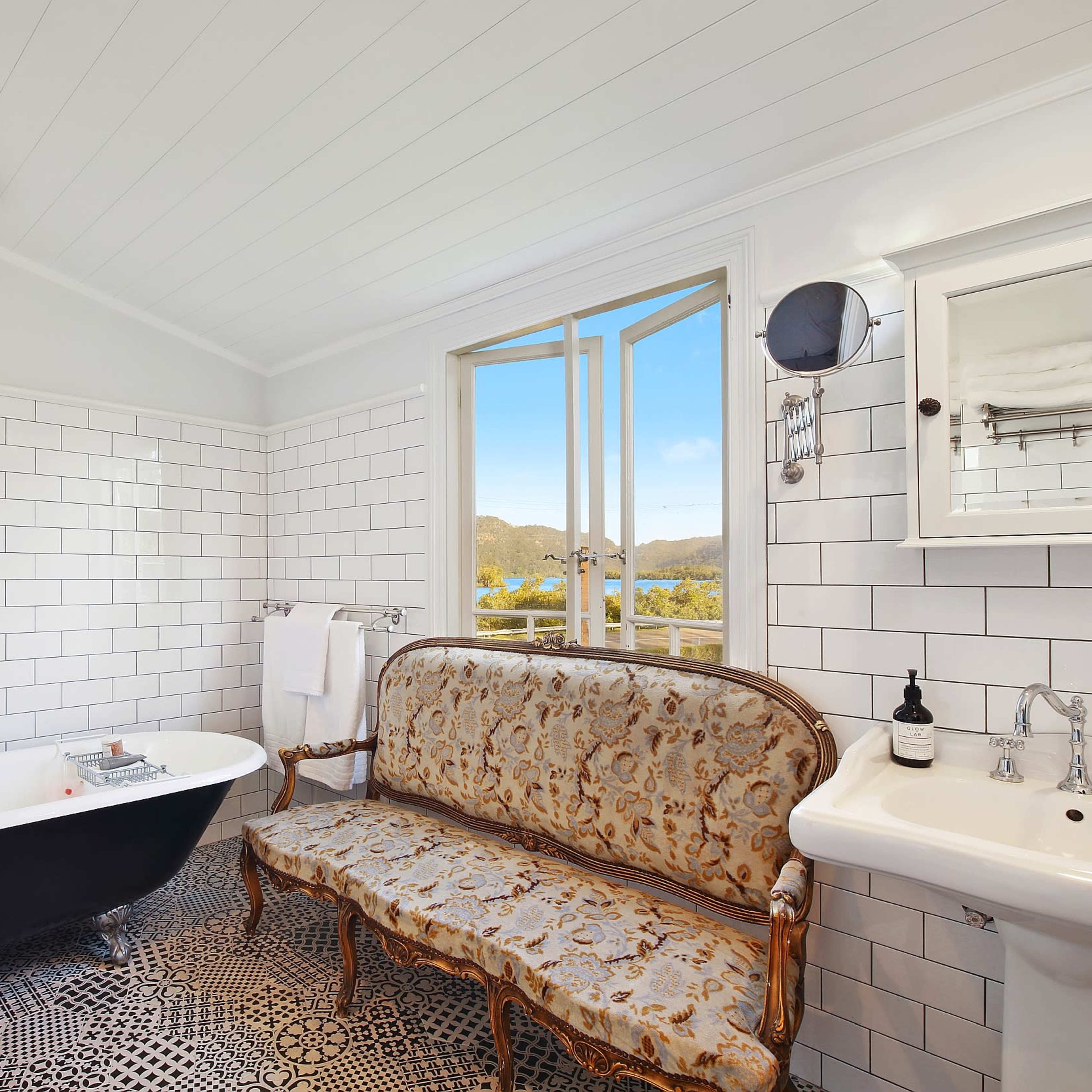 The bathroom features a freestanding black-and-white bathtub, a vintage-style sofa, and a sink beneath a window with scenic views.