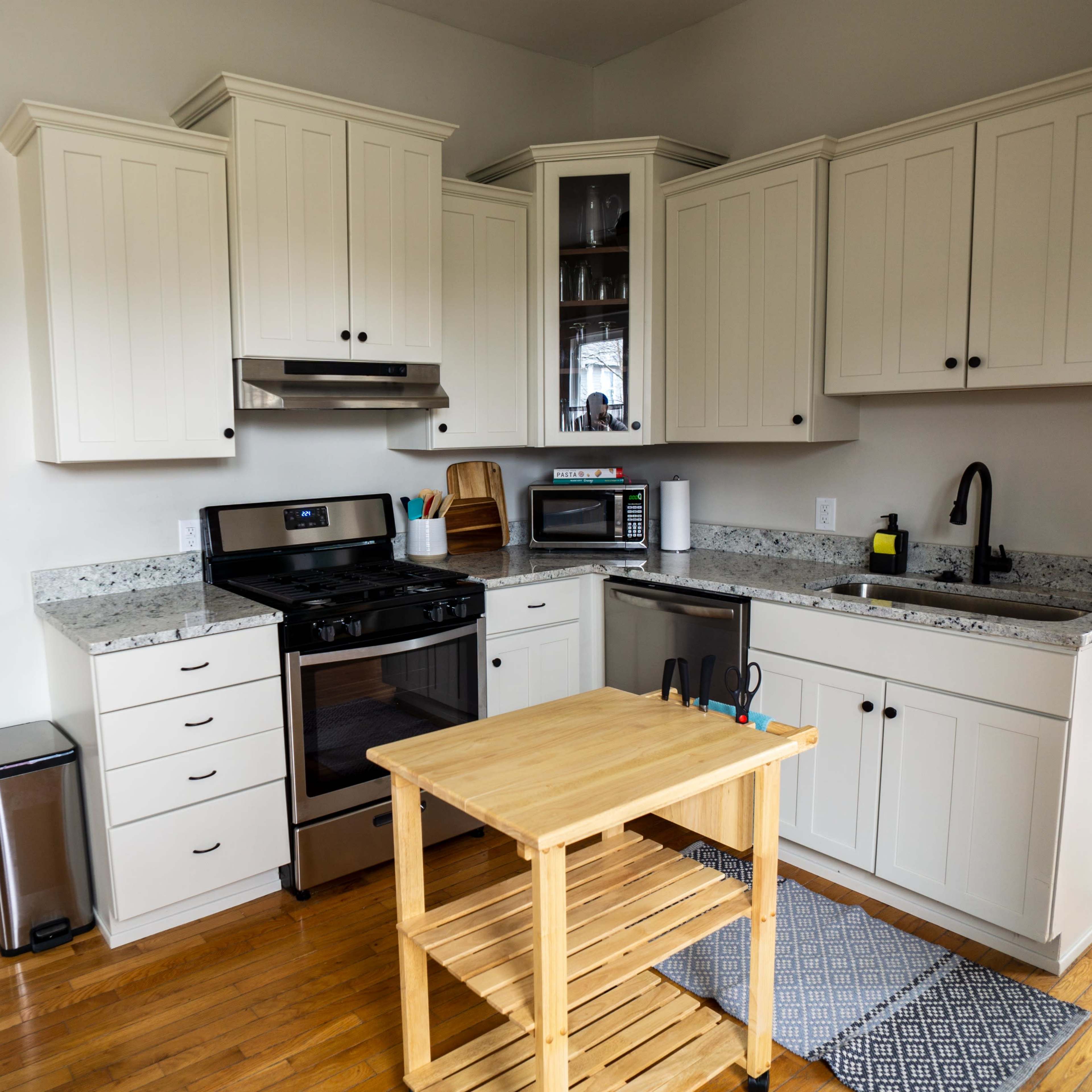 A compact kitchen with white cabinets, a black stove, and a small wooden island on a hardwood floor.