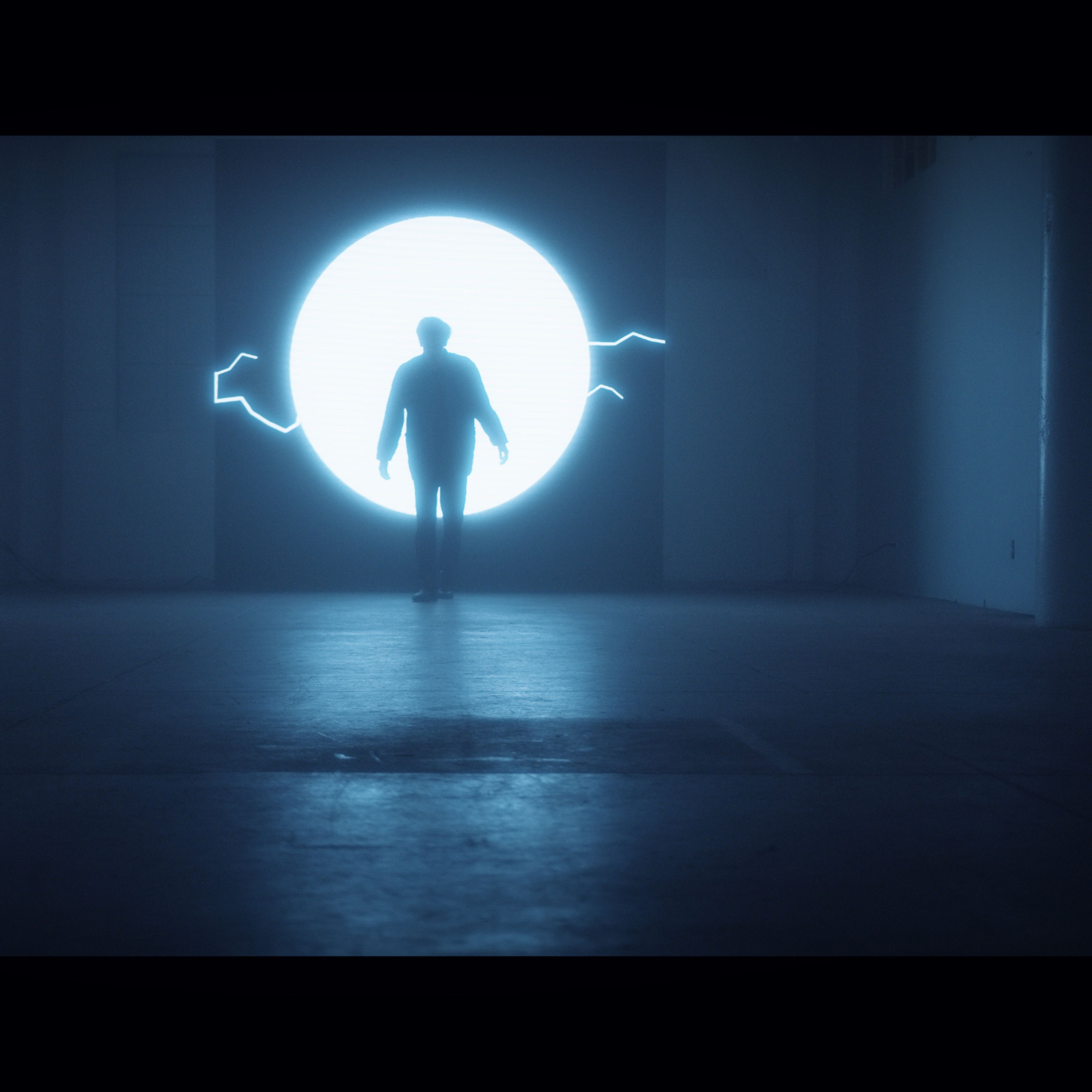 A figure stands in a dimly lit room before a large glowing portal emitting blue light.
