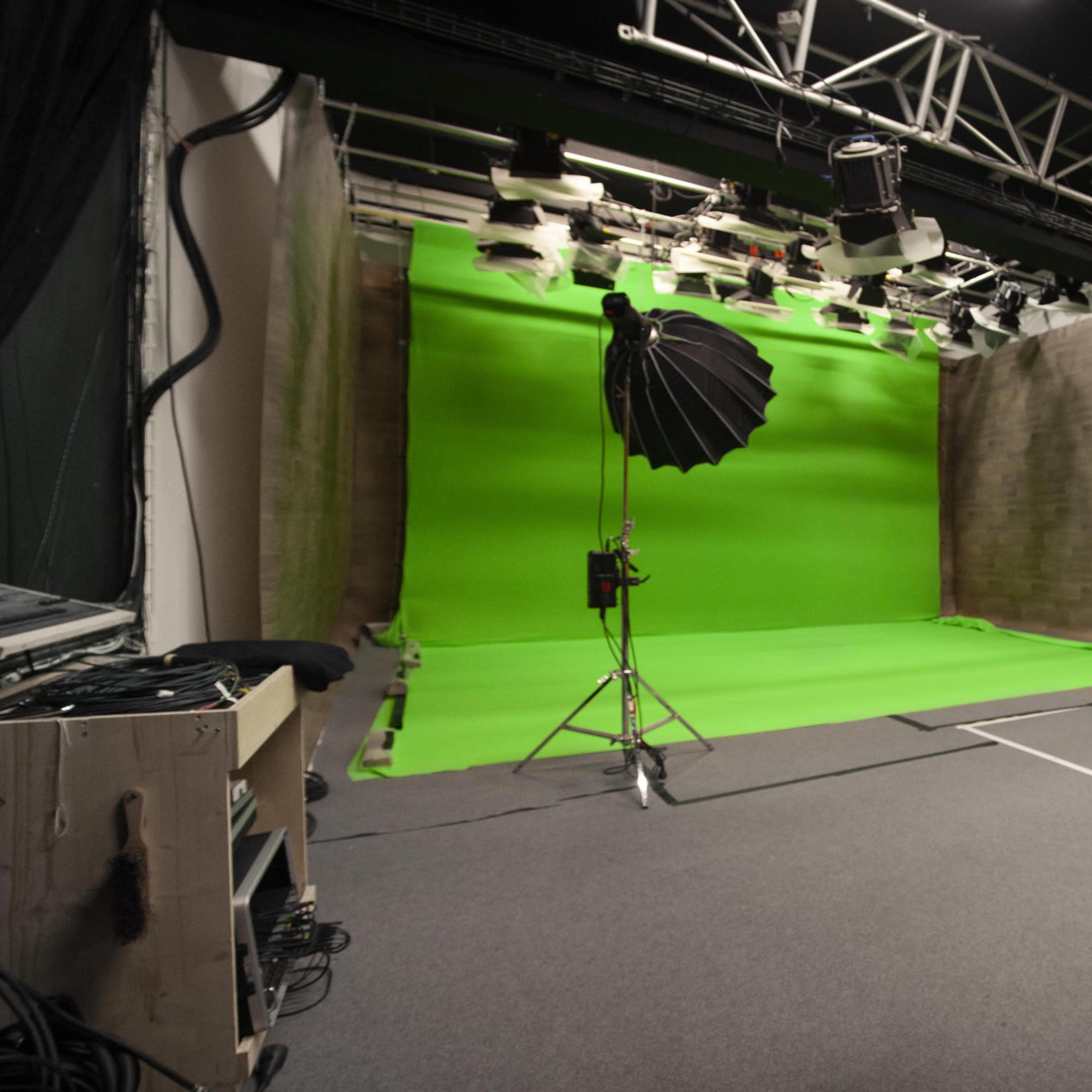 A photography studio featuring a green screen, a yellow backdrop, a vintage sofa, and professional lighting equipment.