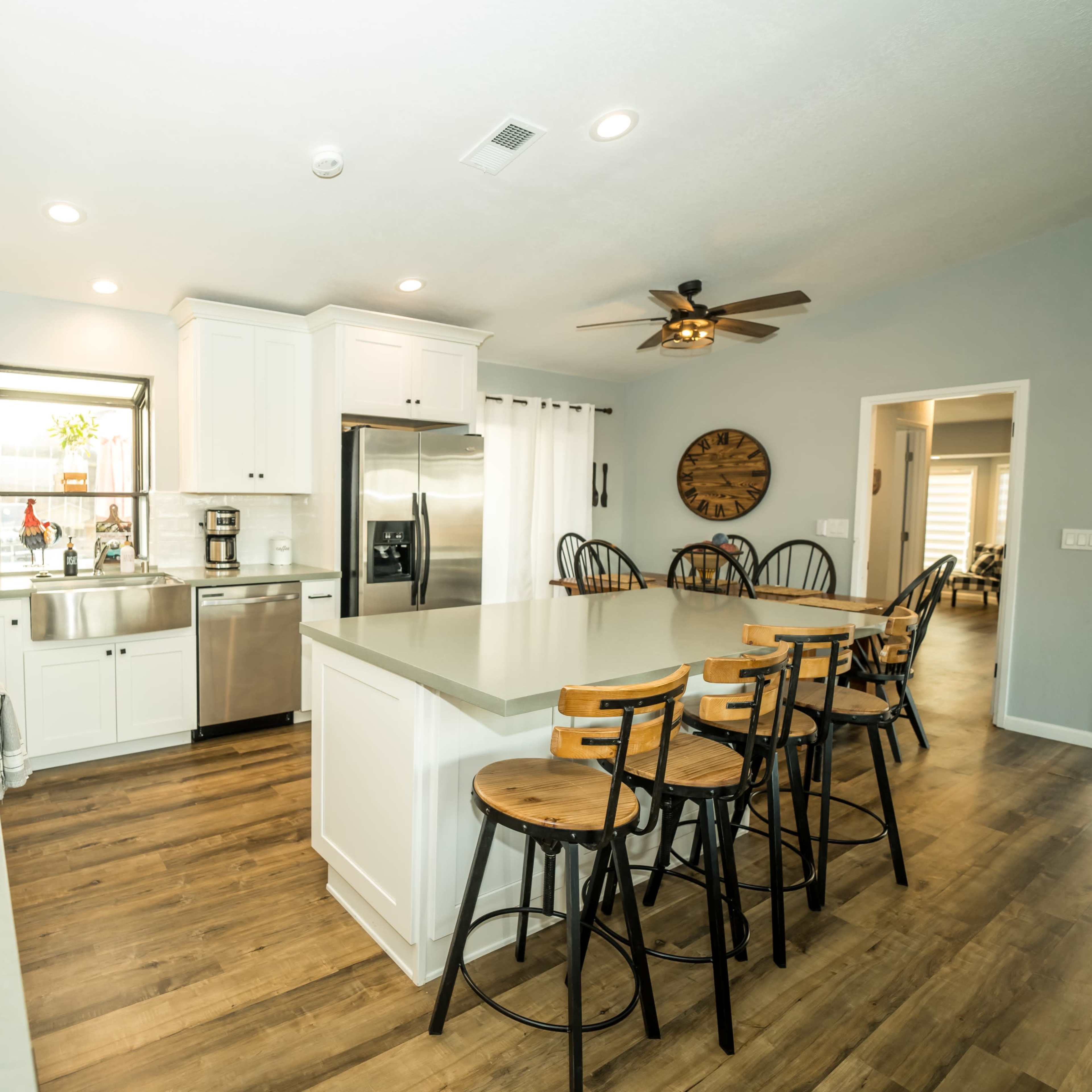 A modern kitchen features white cabinetry, stainless steel appliances, and a central island with barstools, complemented by wood flooring.