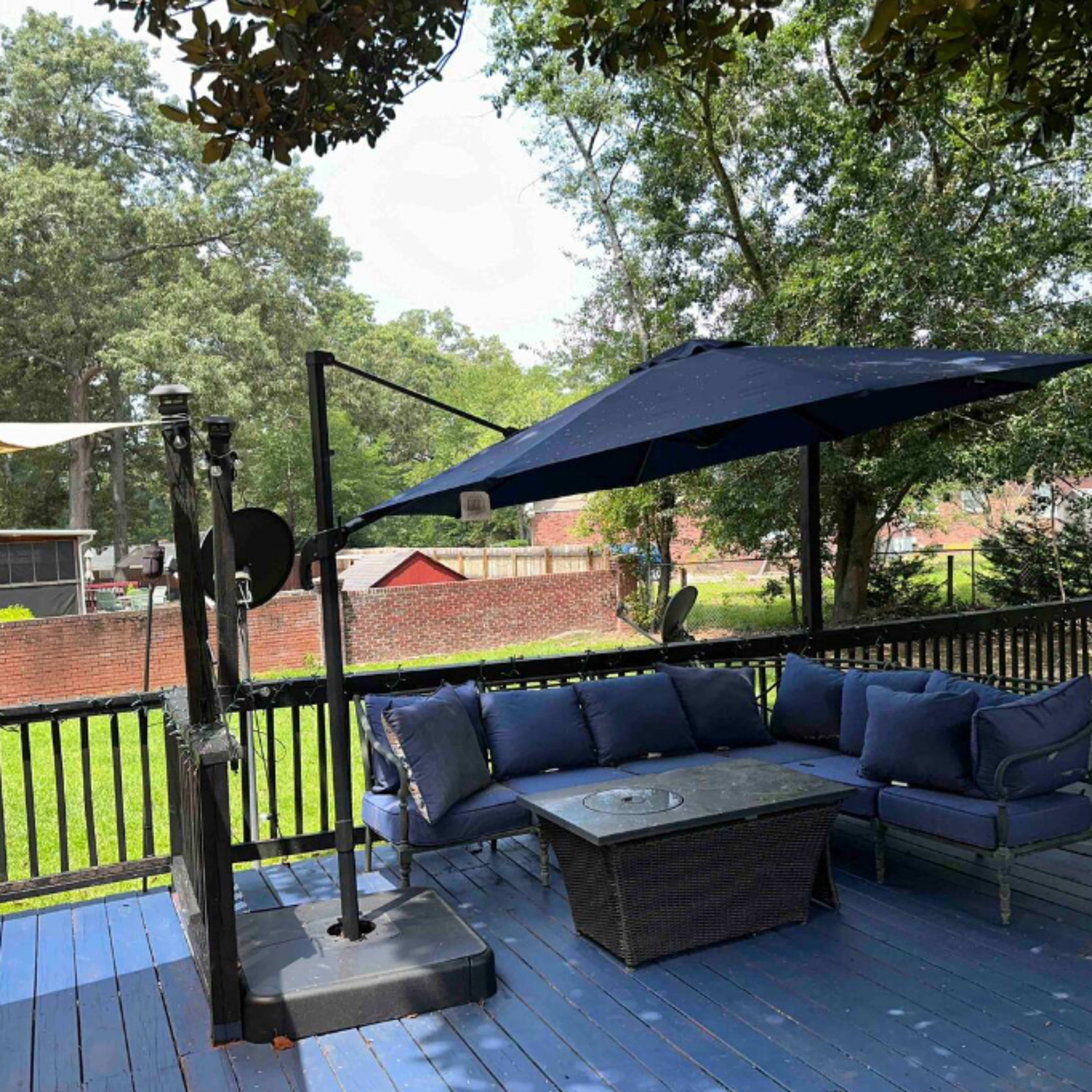 A shaded outdoor seating area with a blue couch and table overlooks a landscaped backyard.