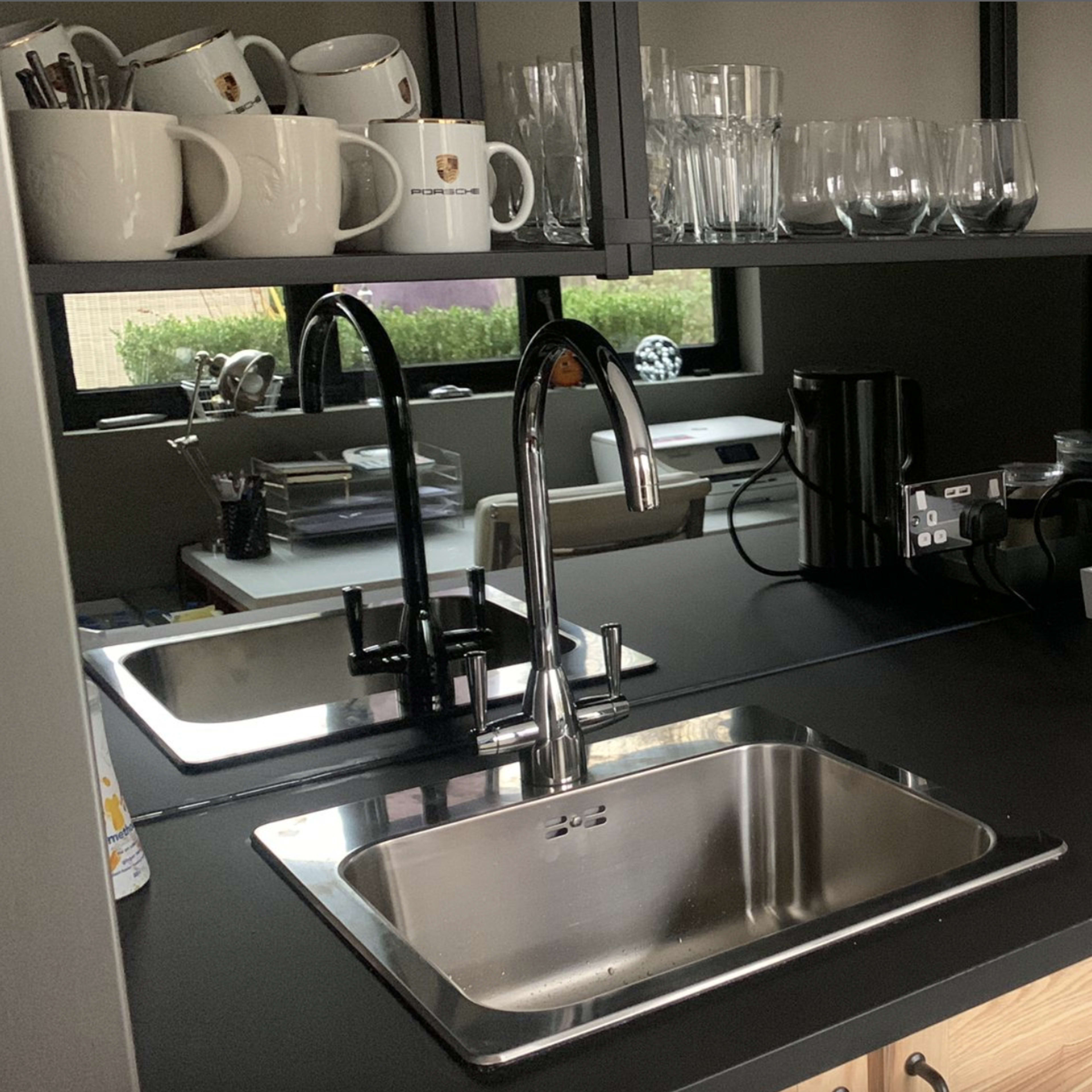 A modern kitchen with a stainless steel sink, a coffee machine, a kettle, and a variety of glassware arranged on open shelves.