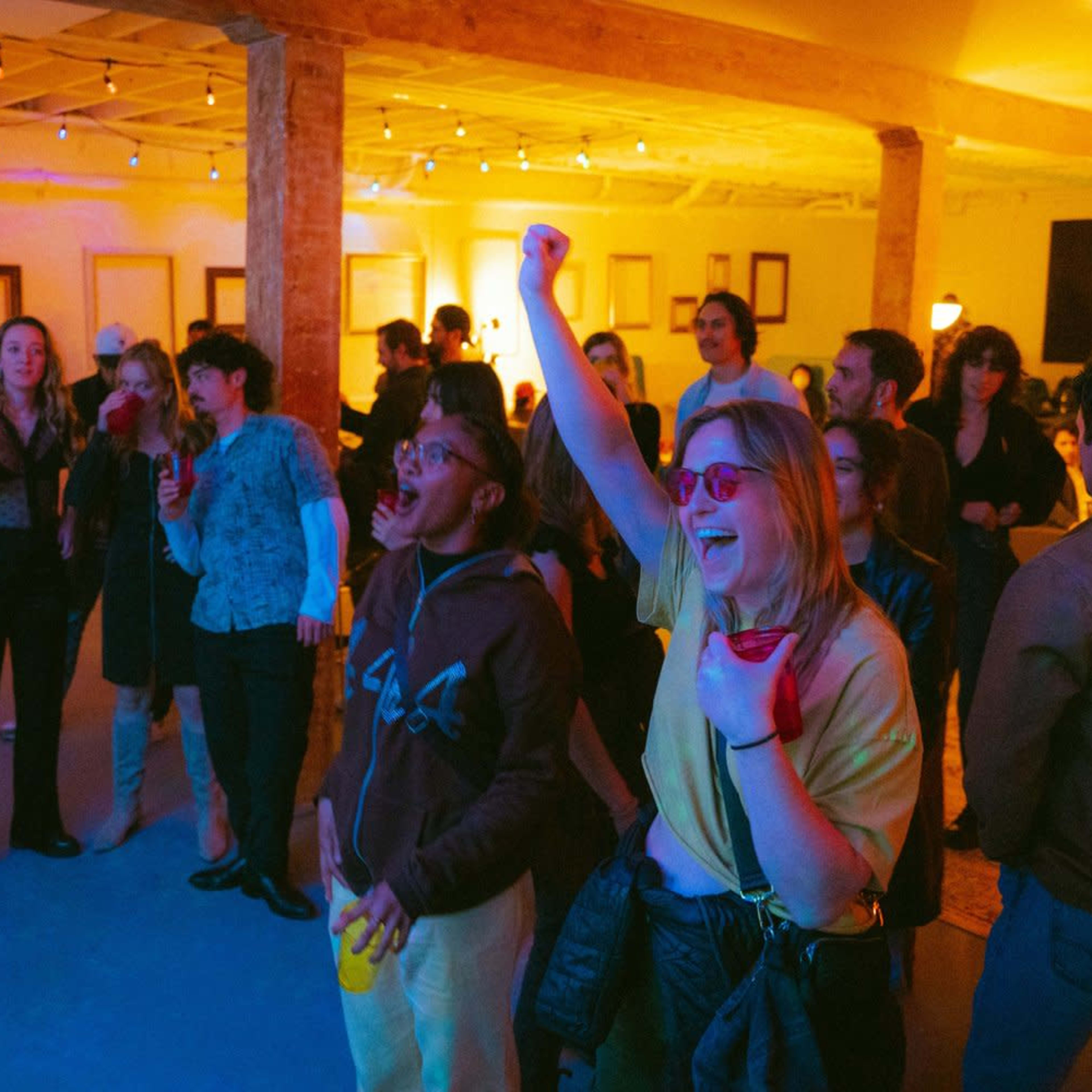 A crowd of people is enjoying a lively indoor party with colorful lighting, engaged in music and conversation.